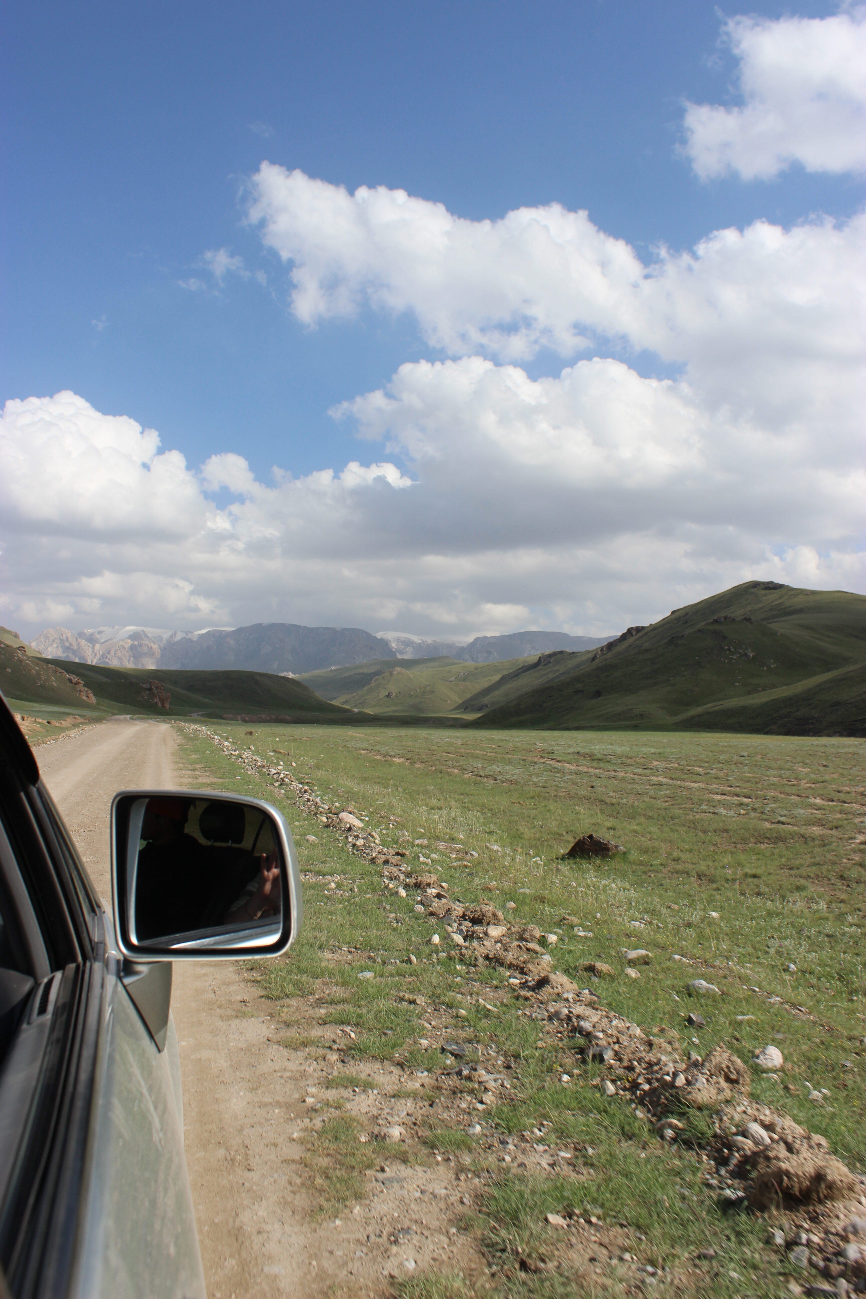 A car side mirror with a view of the road to Kok Kiya valley.