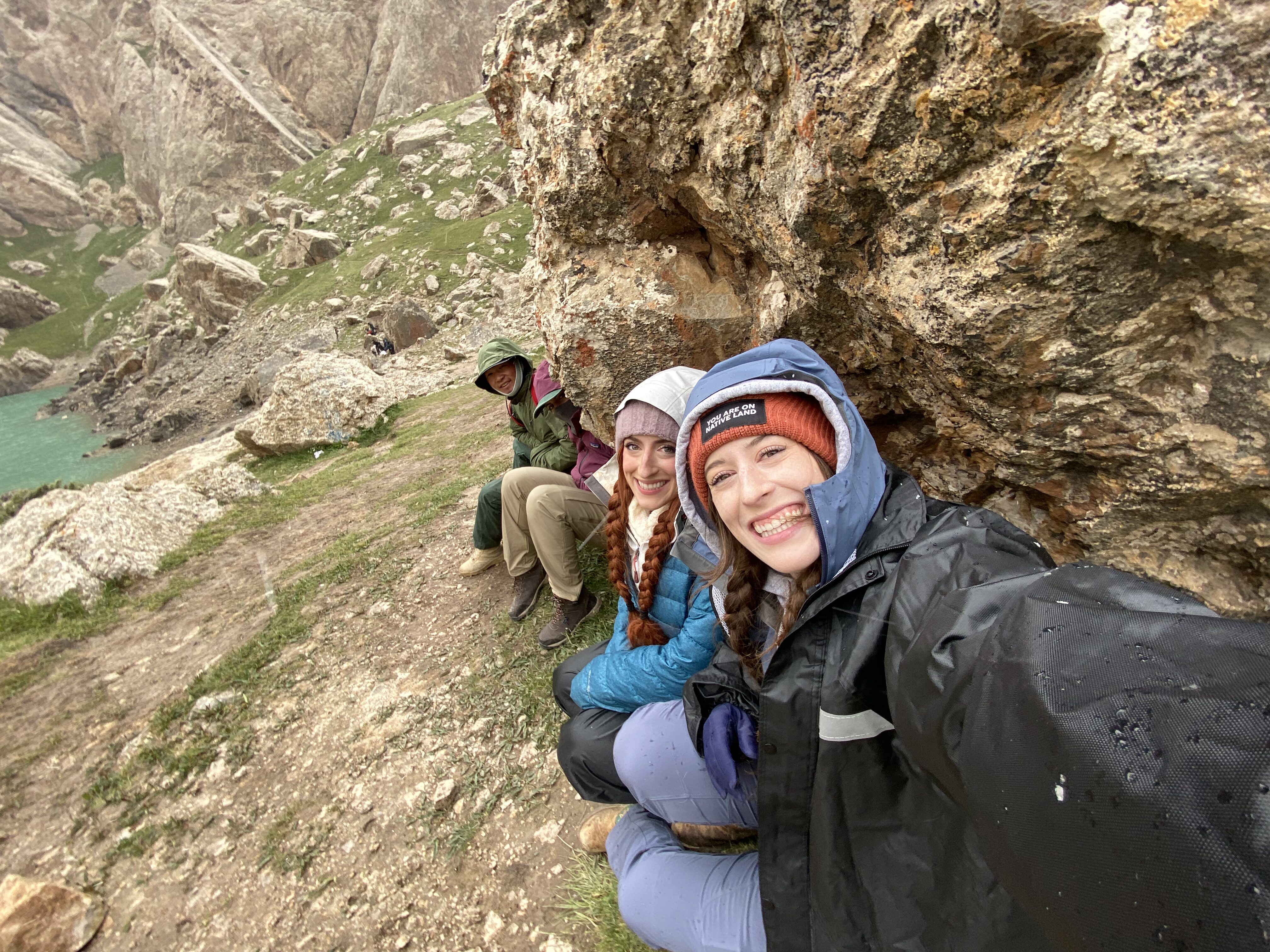A group of people hovering under a rock to take shelter from the rain at Kel Suu.