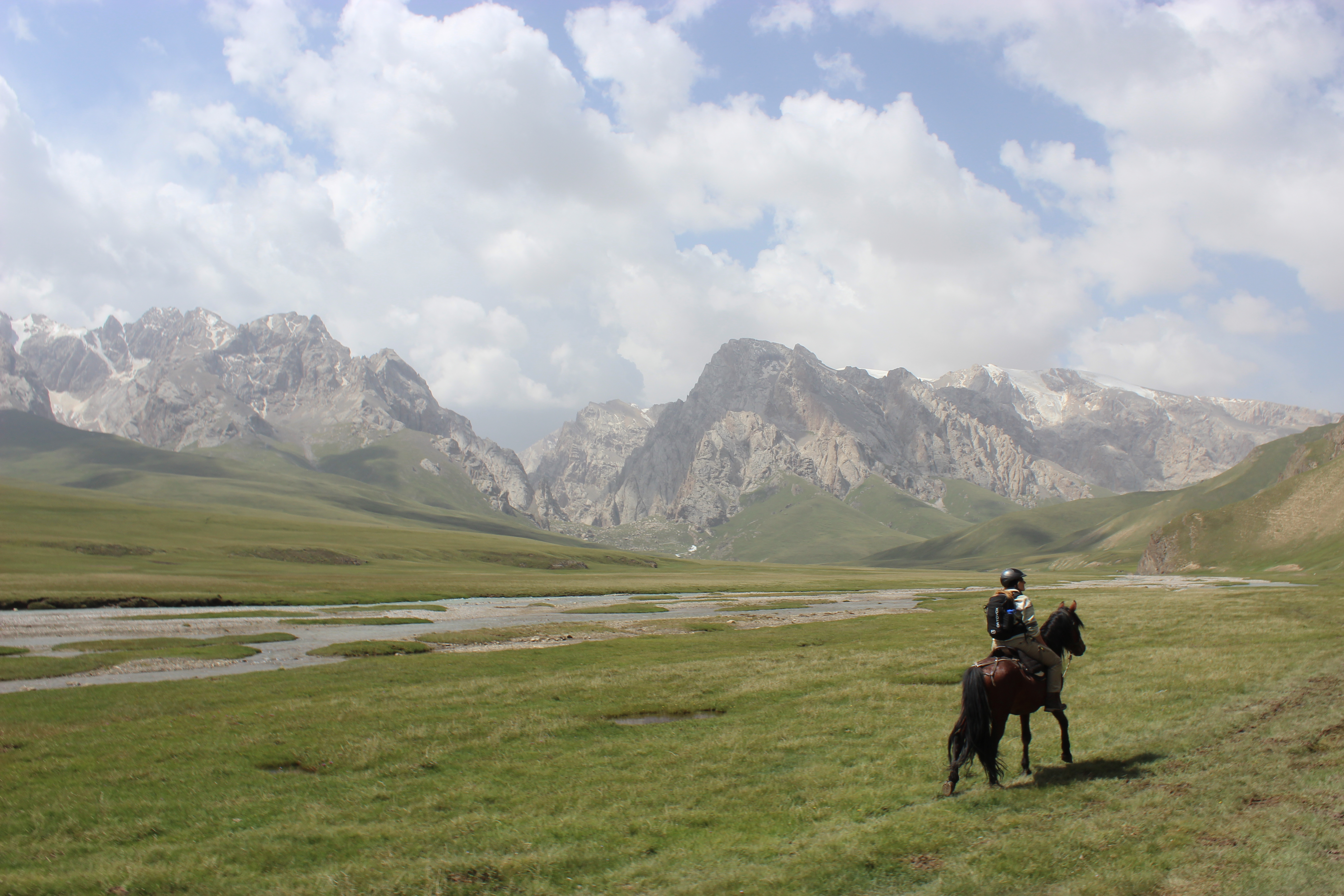 A horseback rider traversing the grassy plains towards the jagged mountains that tower over Kel Suu.