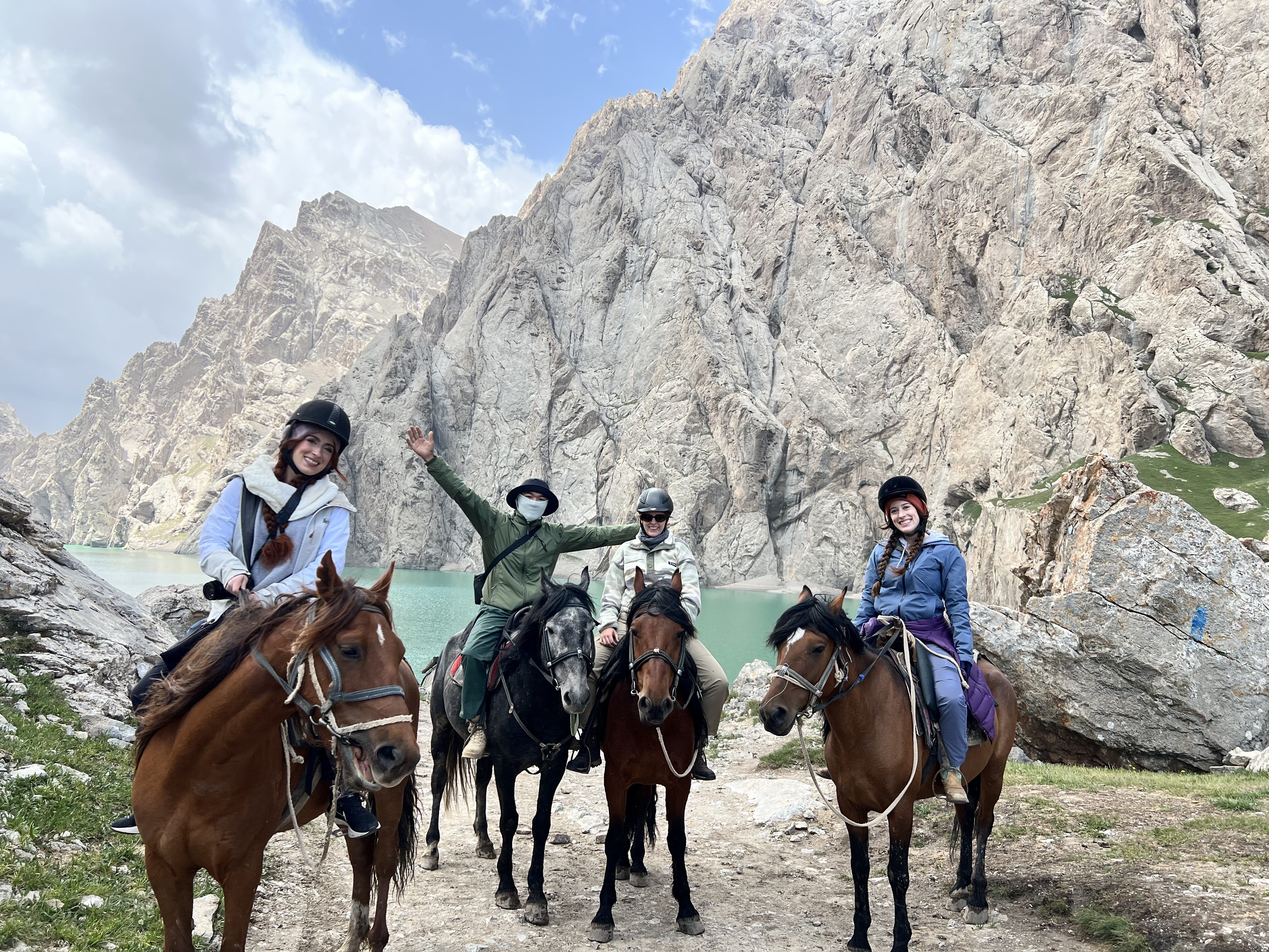A group of four people on horseback in front of the magnificent Kel Suu lake.