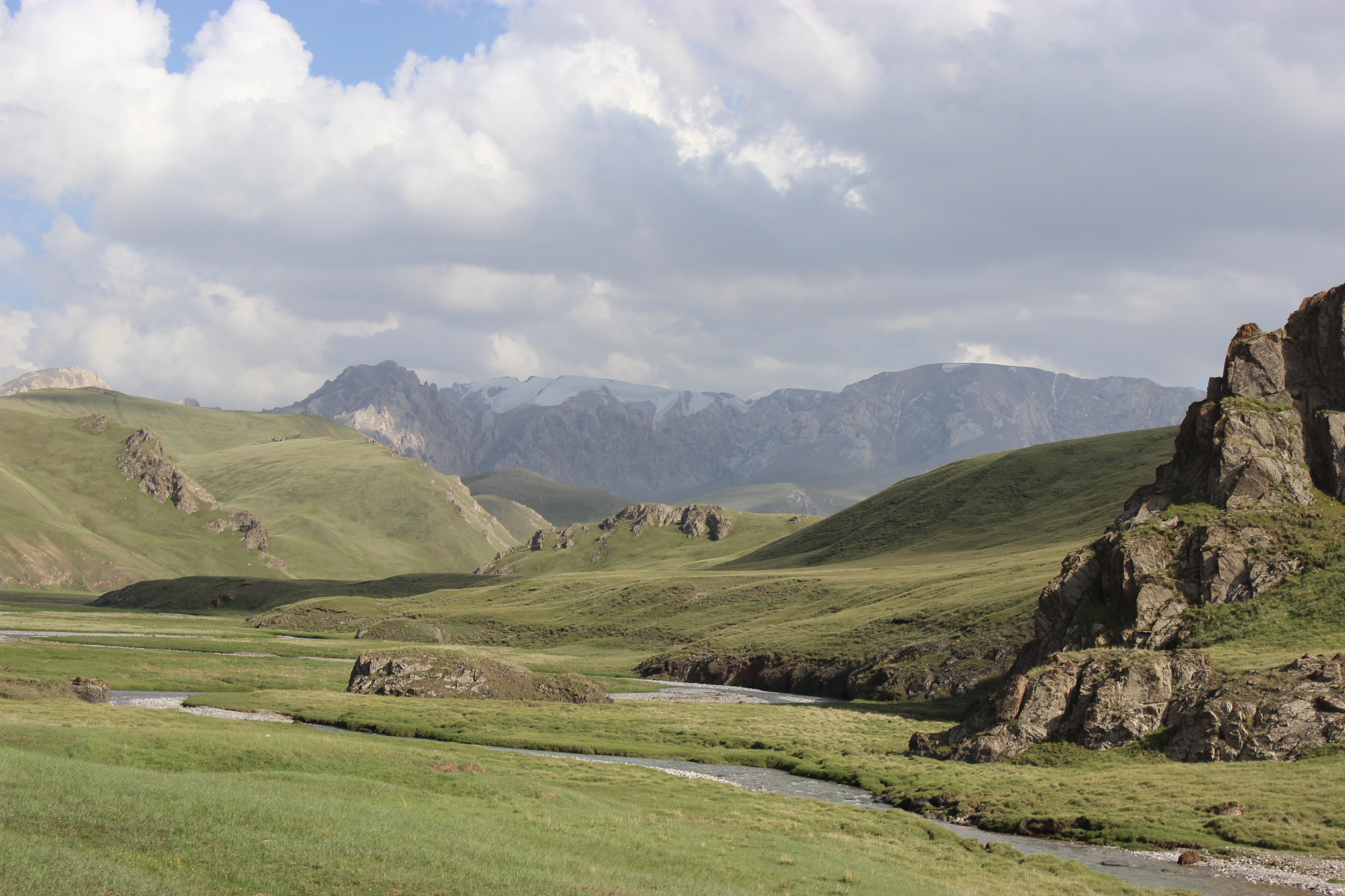 Green hillsides in Kyrgyzstan with beautiful mountains in the background.