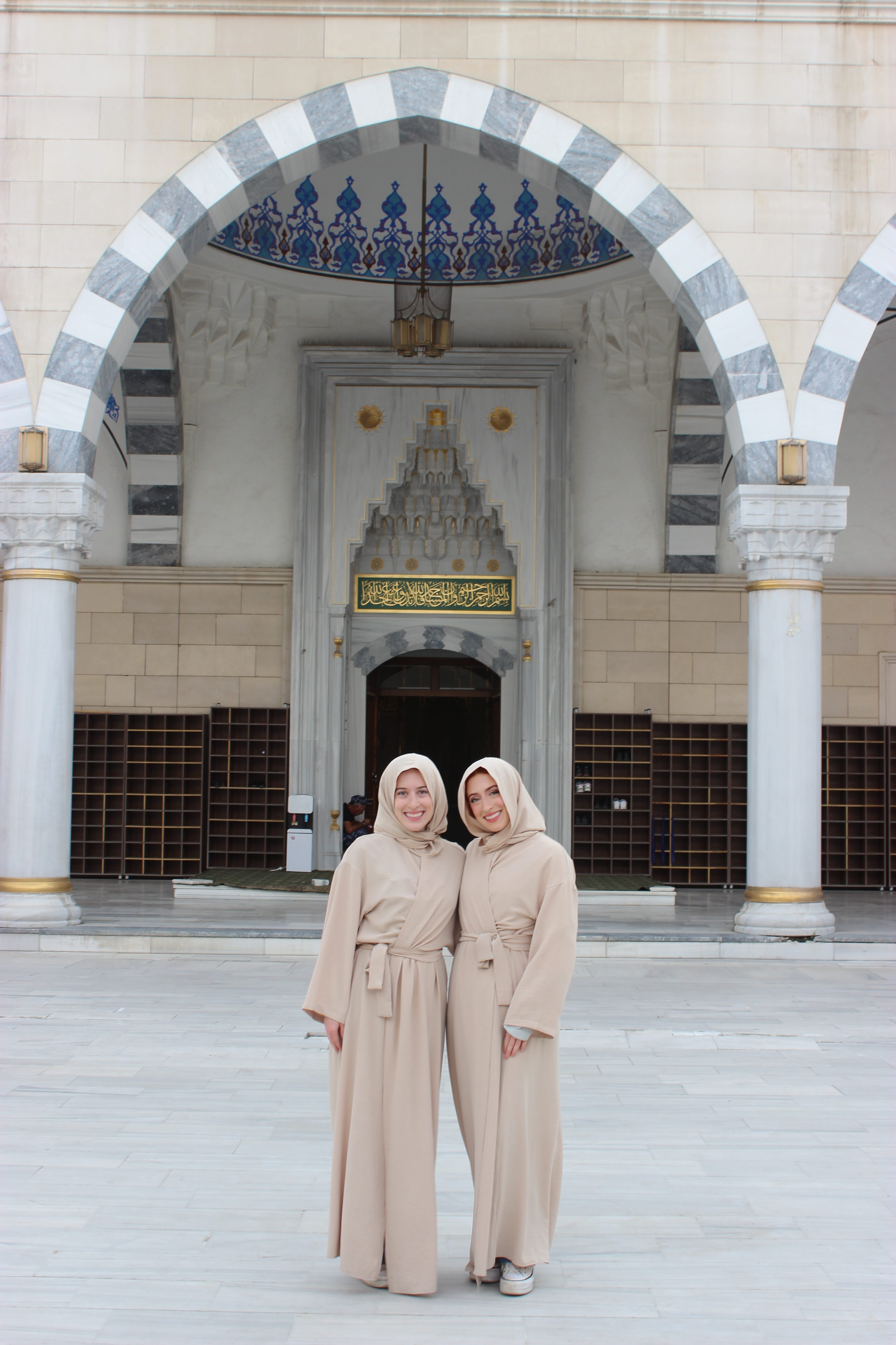 Bella and Lily wearing head and body coverings in front of the entrance of the Bishkek Central Mosque.