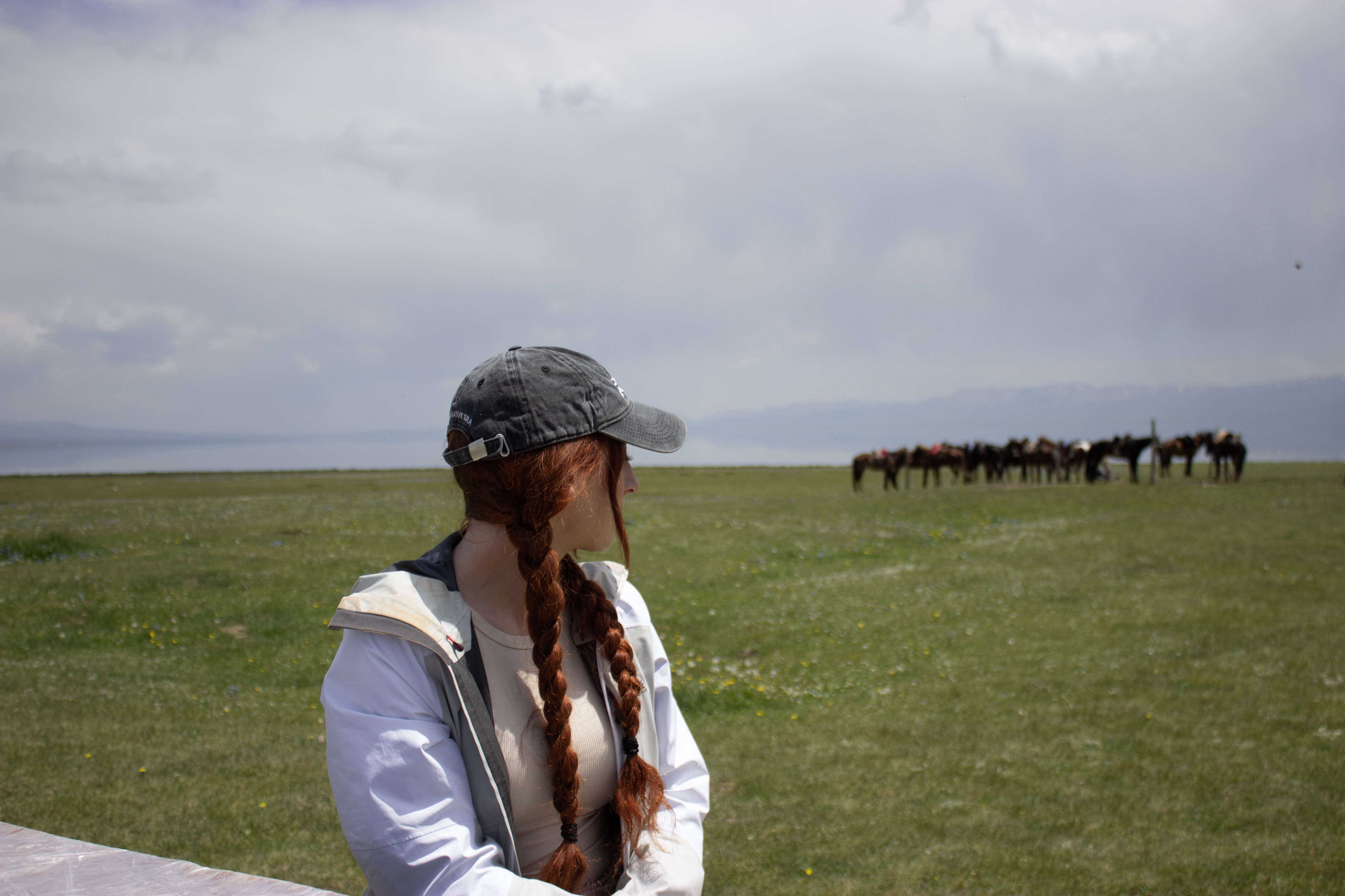Lily looking into the distance, towards a herd of horses and Song Kul lake in the background.
