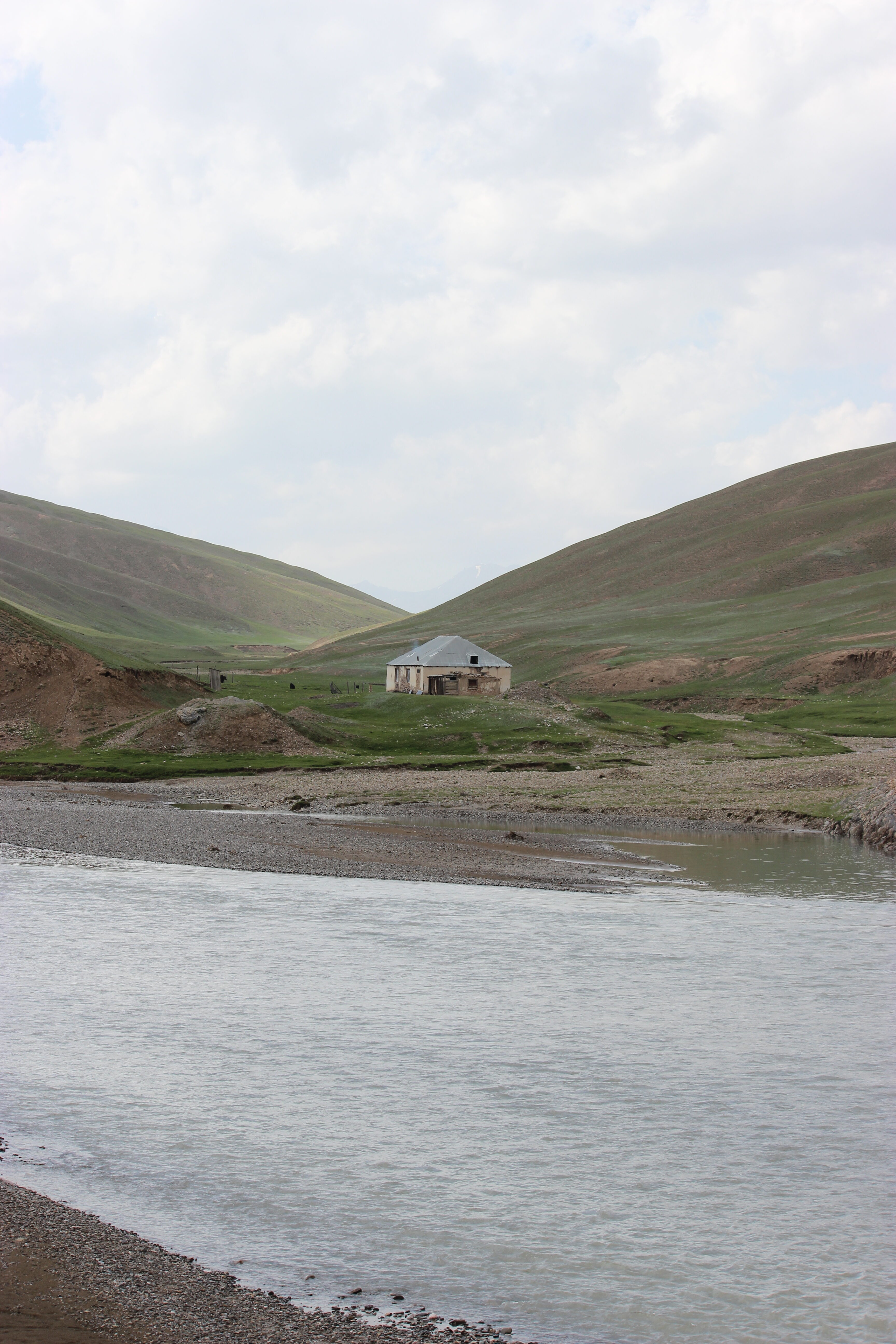 A house among the grassy hills across the river – one of Kyrgyzstan's scenic landscapes.