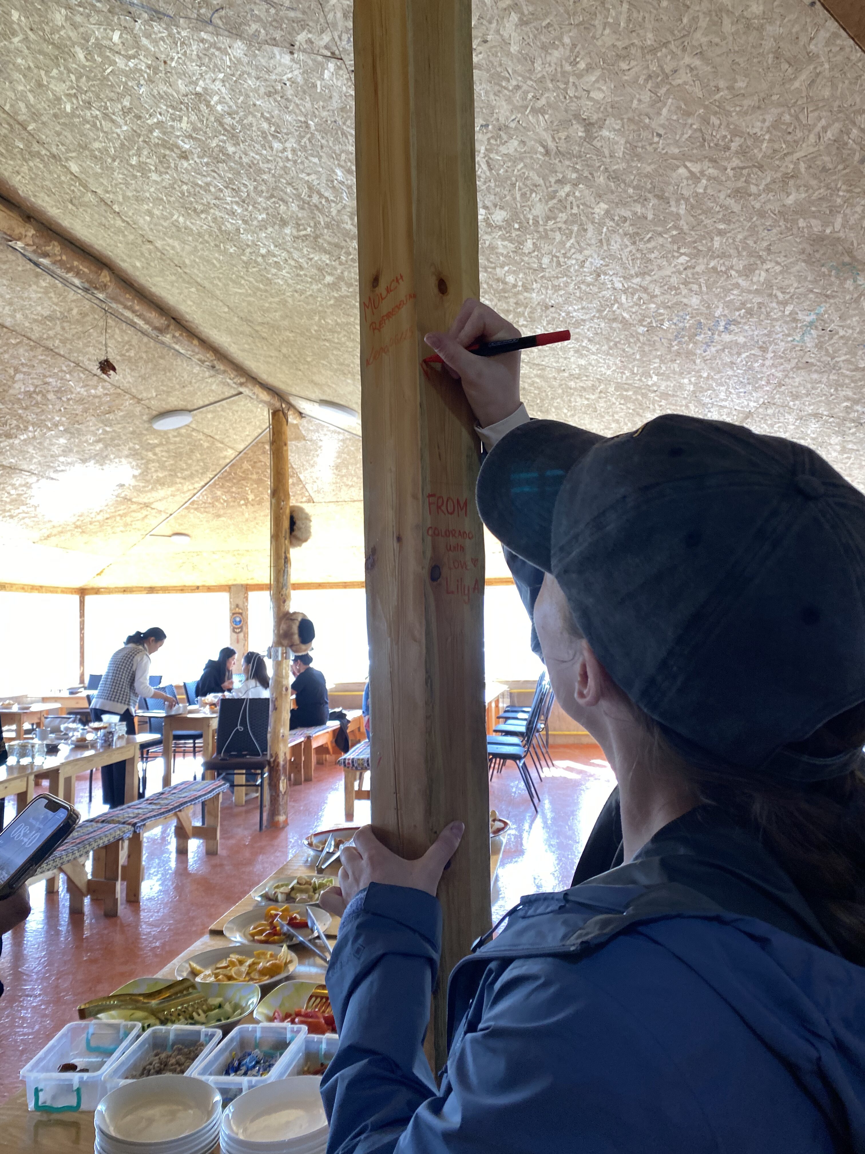 Bella signing a wooden beam in the wooden dining hall of Jyrgal Yurt Camp and Guesthouse.