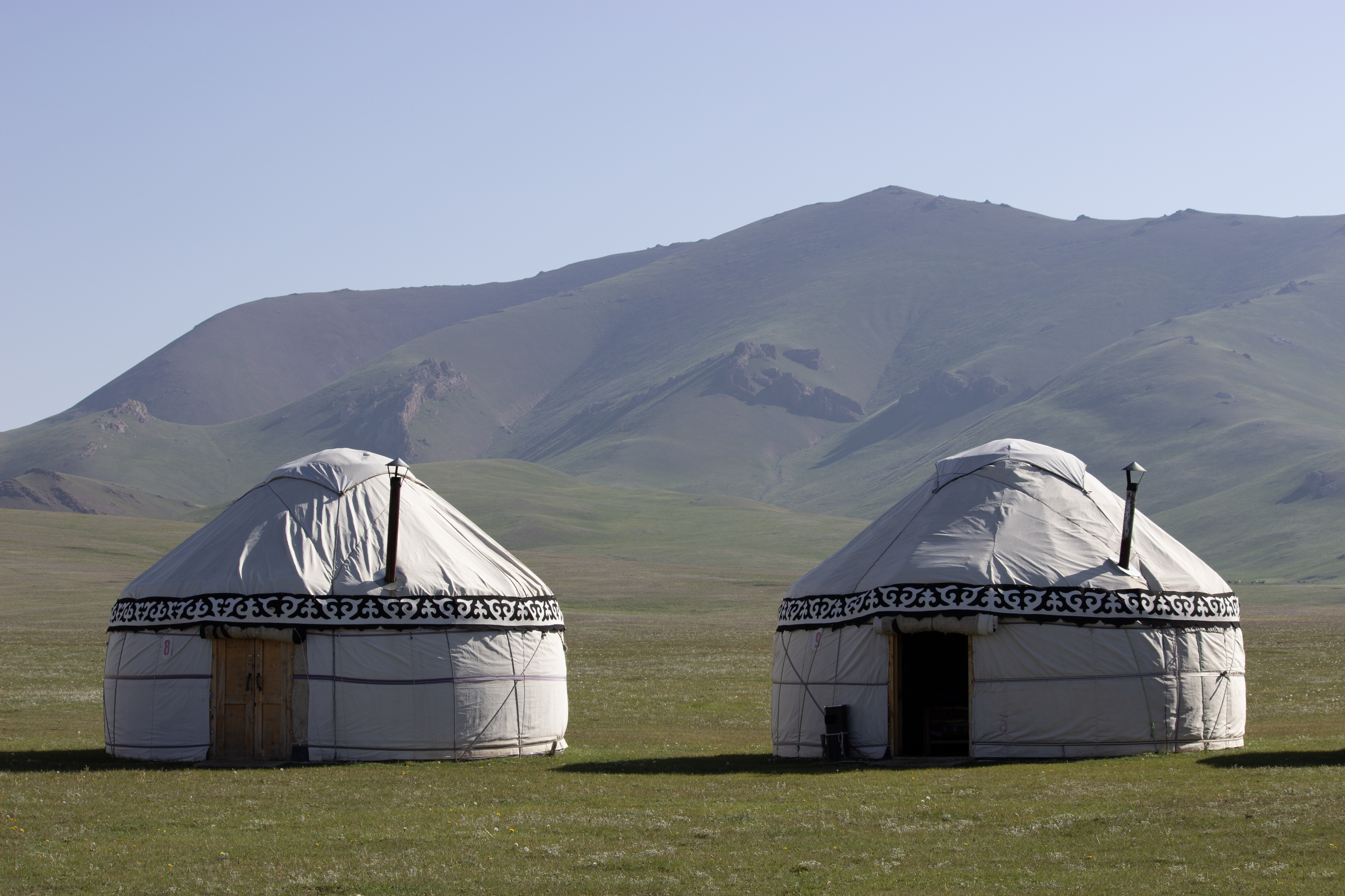 Two yurts in front of a grassy hill at Song Kul lake.