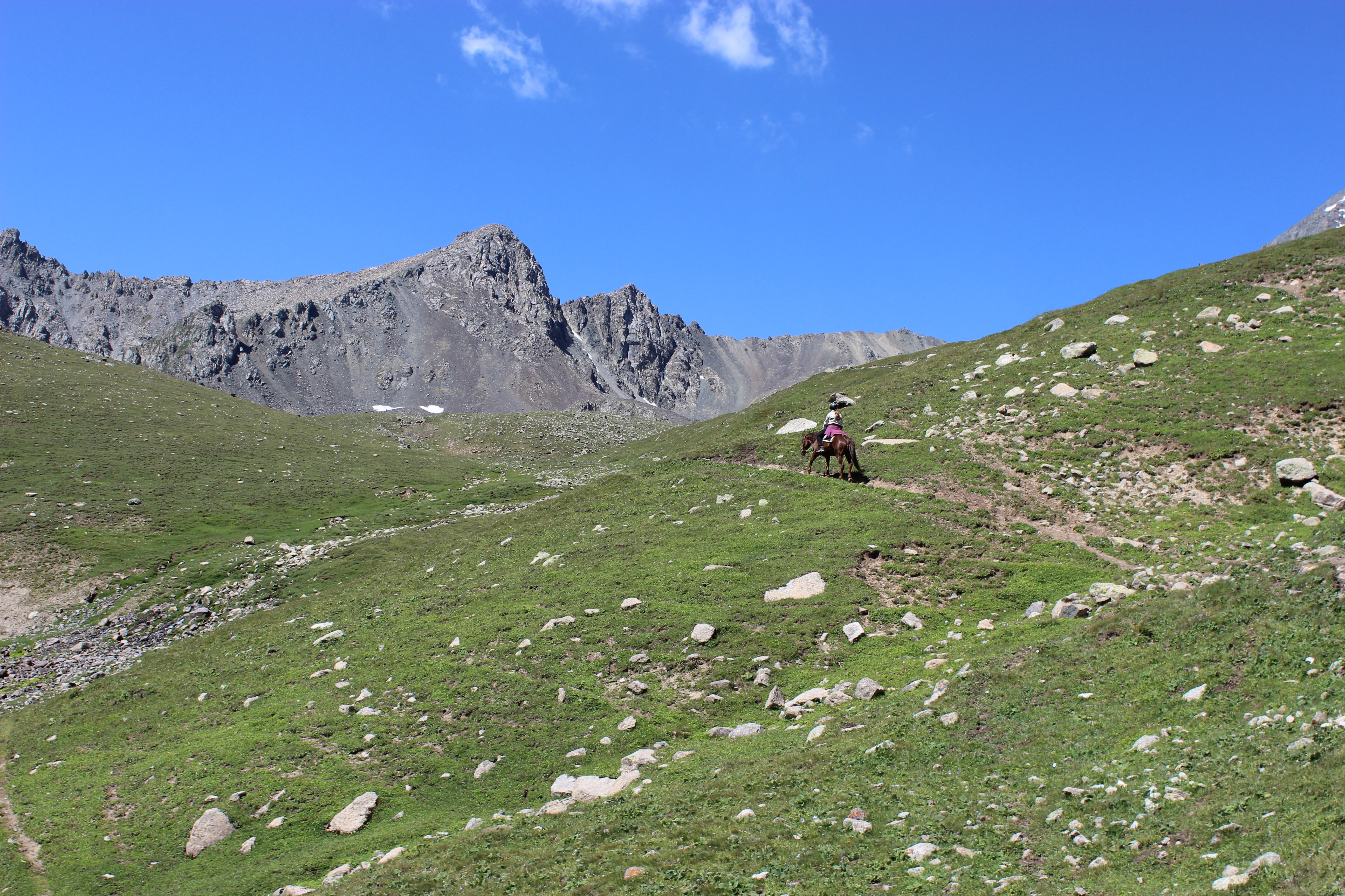 A horseback rider traversing a rocky trail with jagged cliffs in the background.