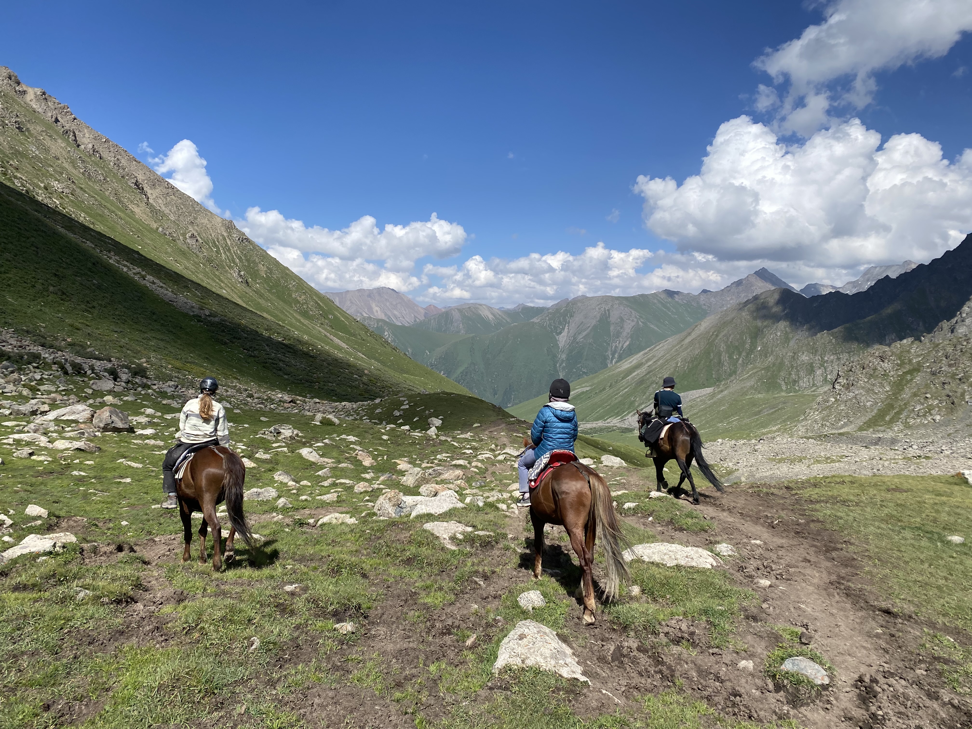 A group of horseback riders riding along a rocky hillside in the Tian Shan mountains outside of Altyn Arashan.