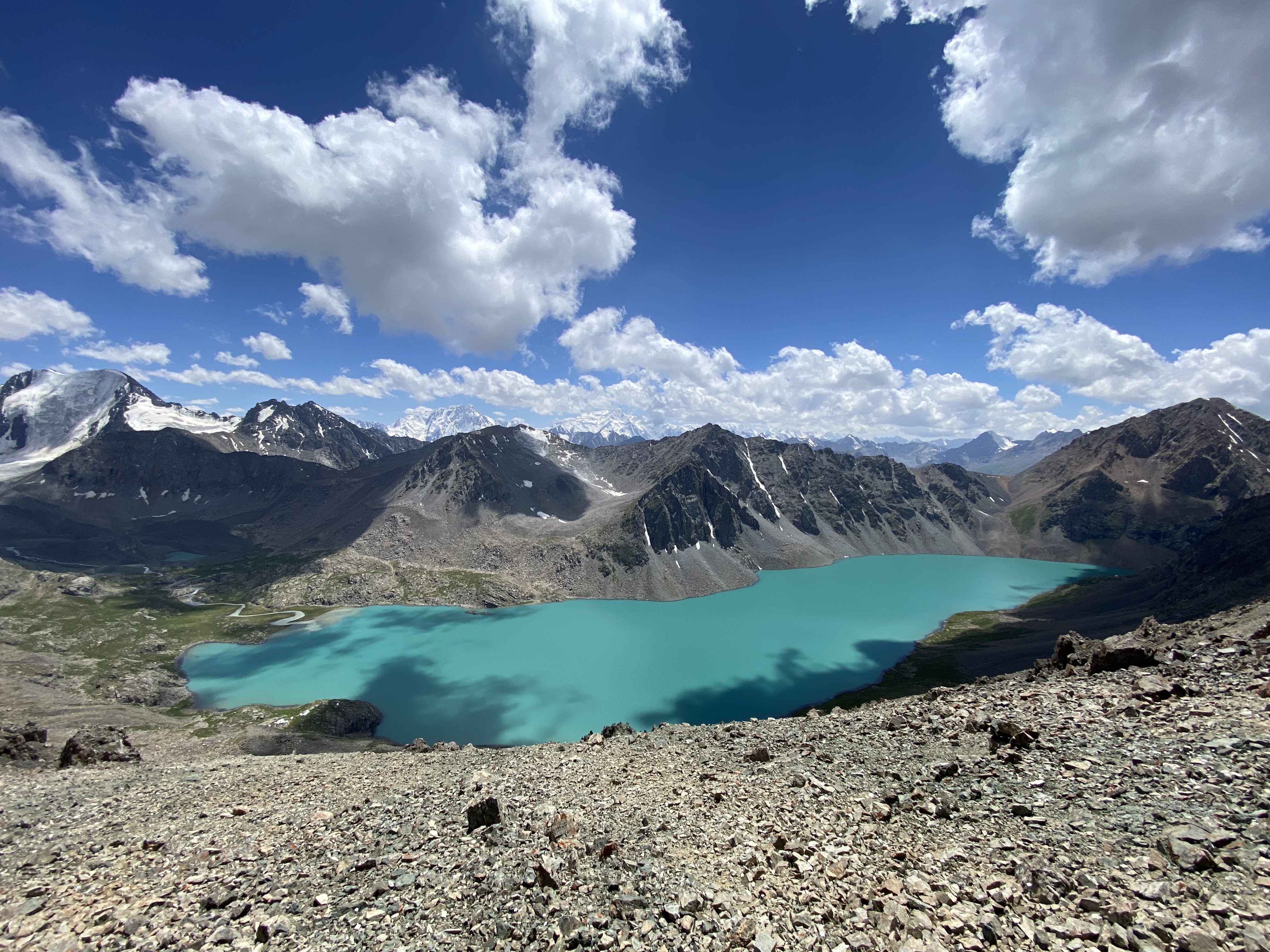 The mesmerizing, turquoise alpine lake nestled in the rocky grey mountains of Kyrgyzstan. Ala Kul sits beneath a cloudy, blue sky.