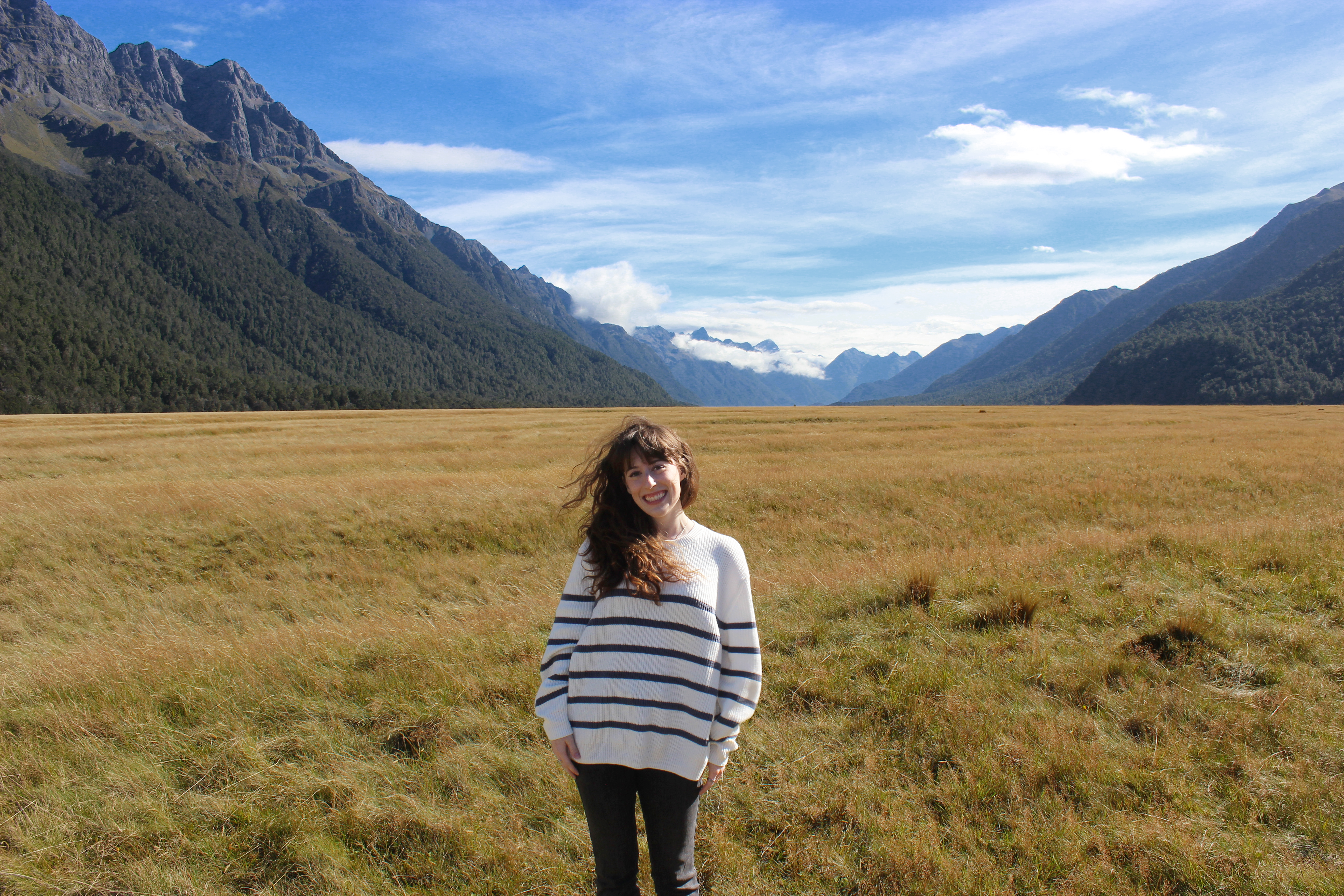 A young woman wearing a striped white sweater and black jeans standing in Eglinton Valley, a scene from Fellowship of the Rings.