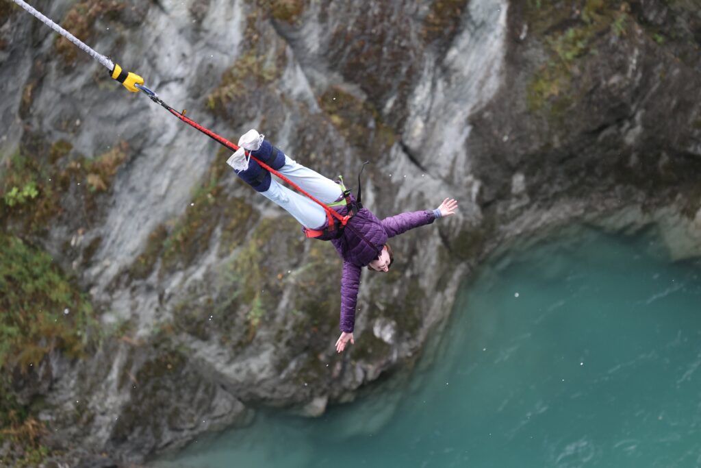 A young woman dangling by her feet via bungee cords over the blue water beneath Kawarau Bridge.