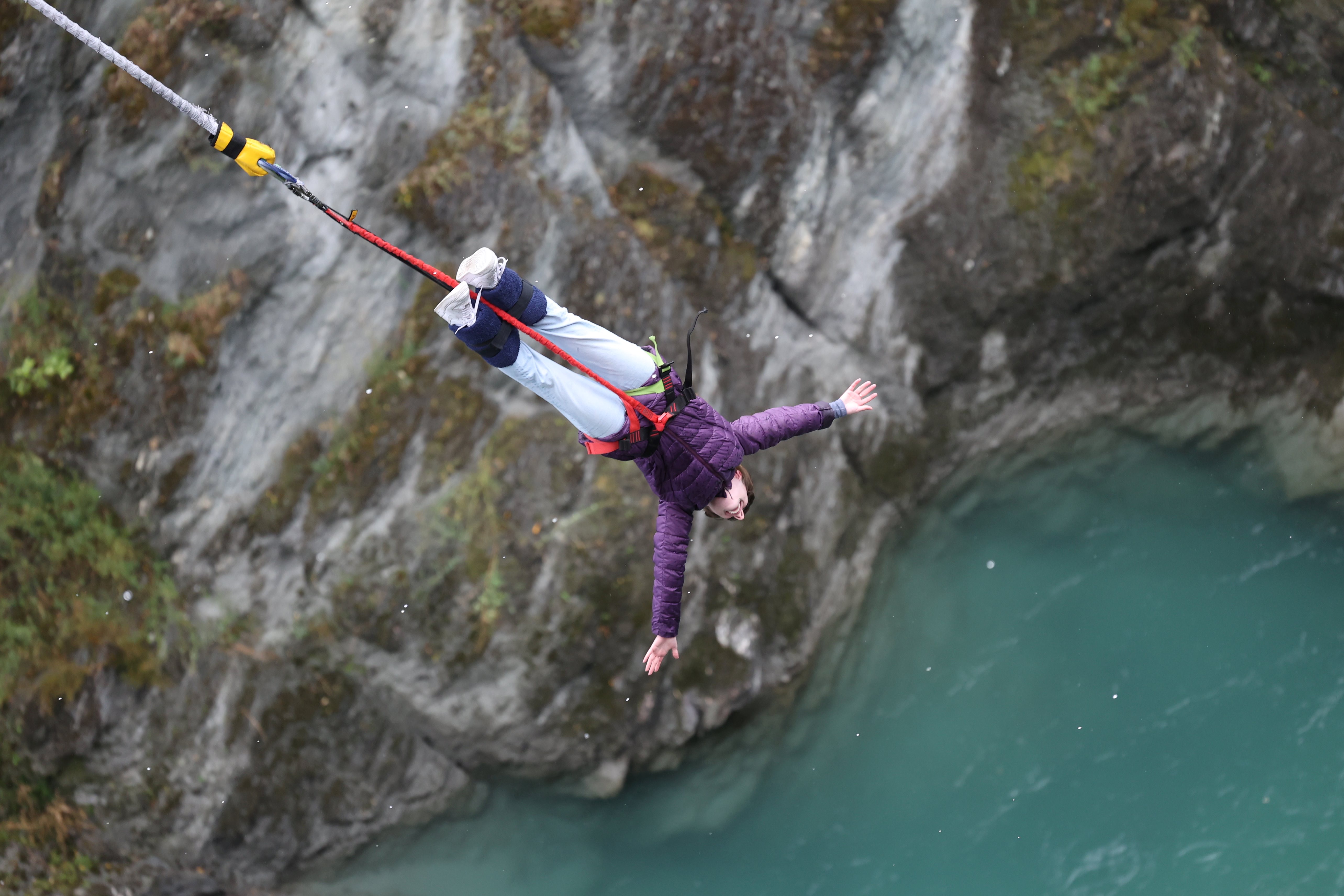 A young woman dangling by her feet via bungee cords over the blue water beneath Kawarau Bridge.