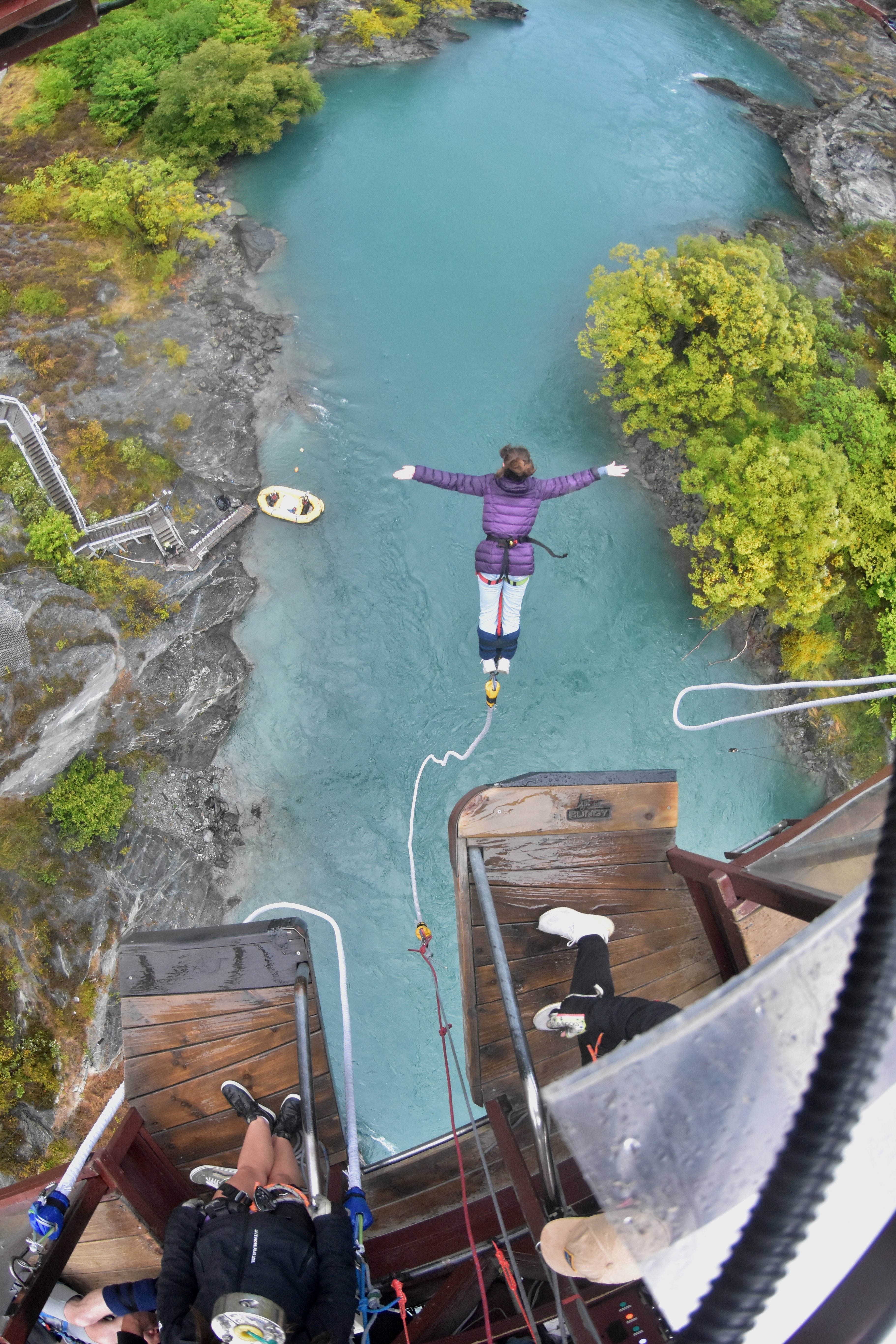 An aerial view of a woman bungee jumping over the turquoise water beneath Kawarau Bridge.
