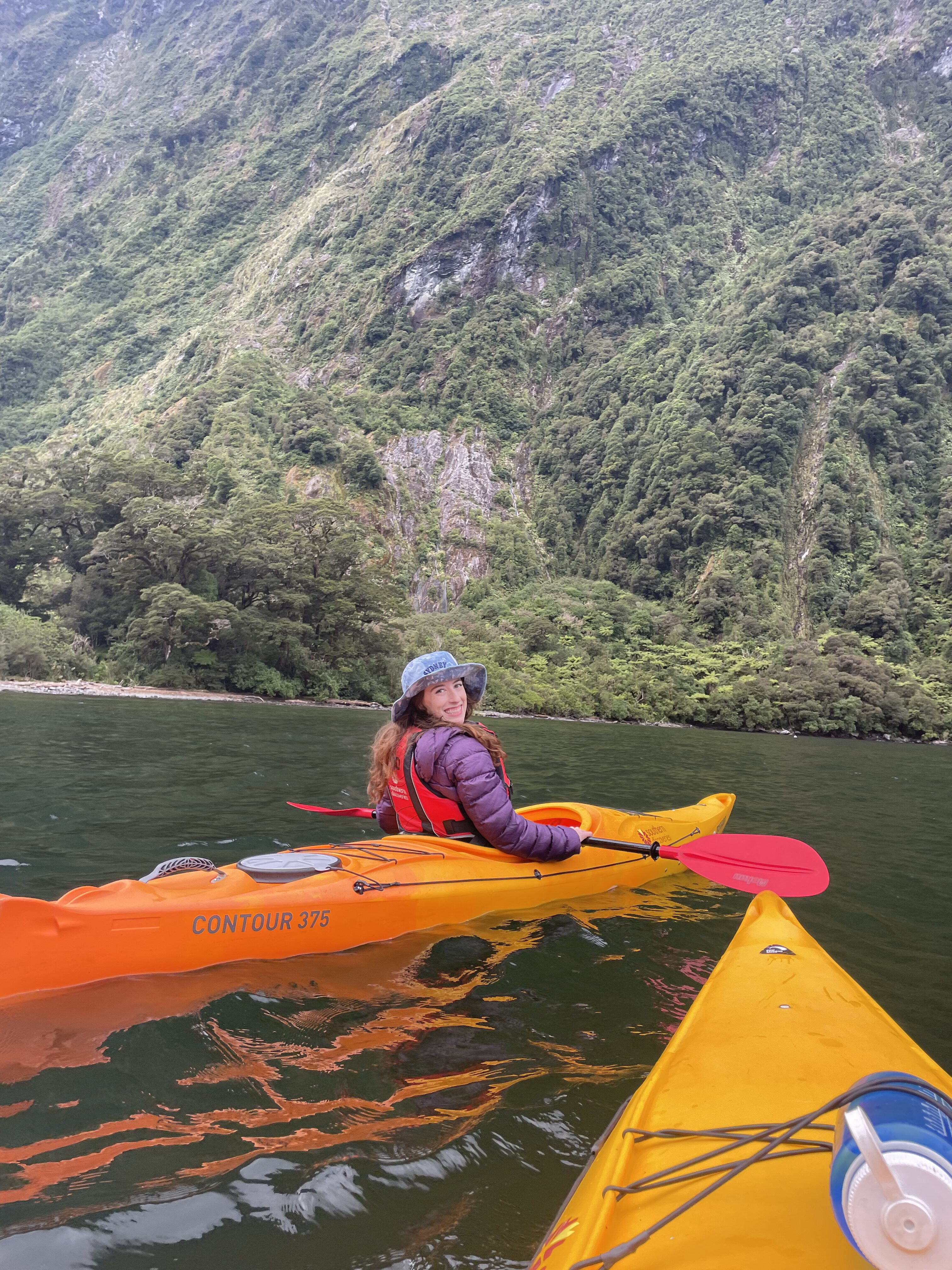 A kayaker sitting an a bright orange kayak on Milford Sound.