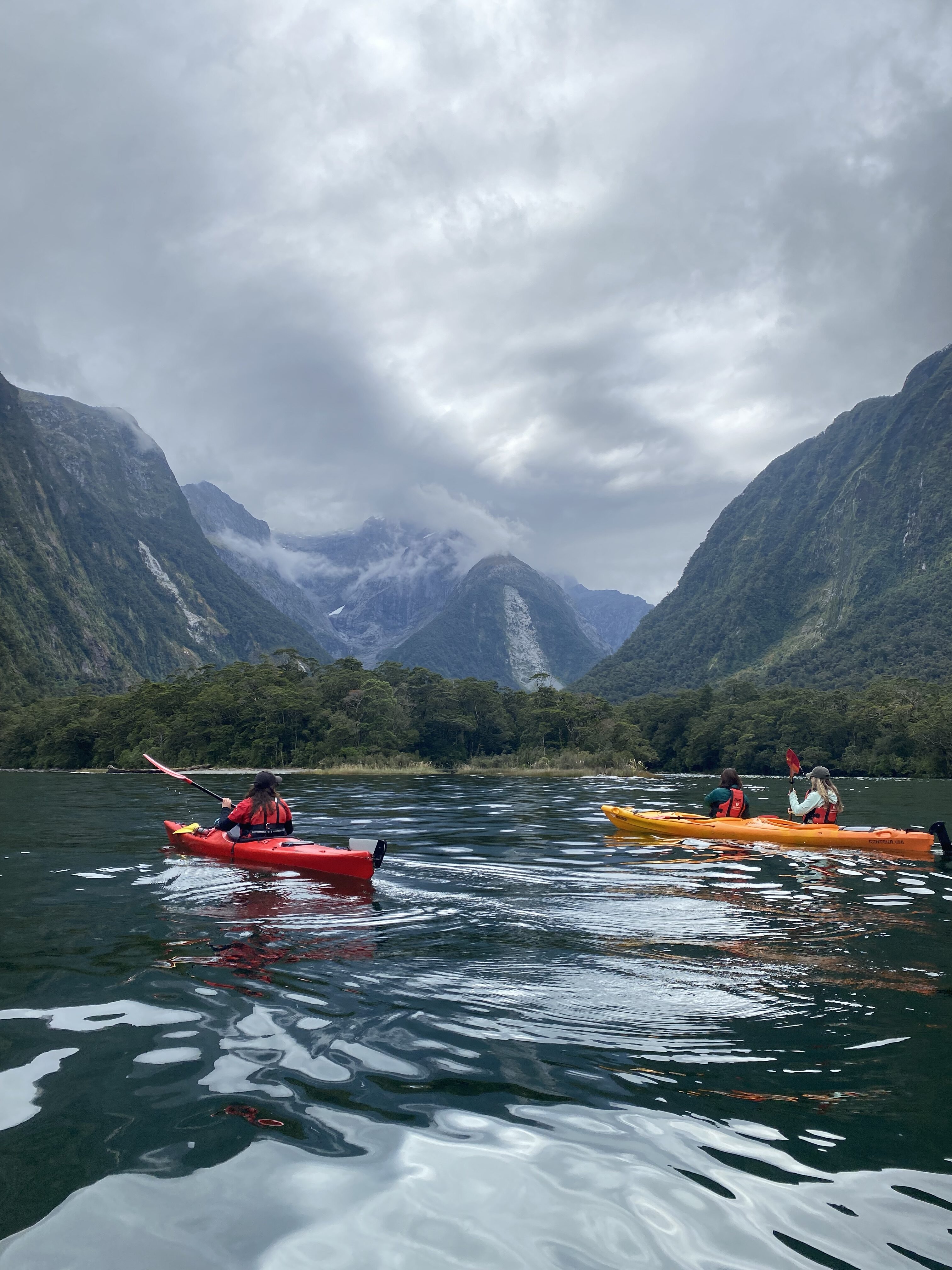 A pair of kayakers paddling along the calm waters of Milford Sound.