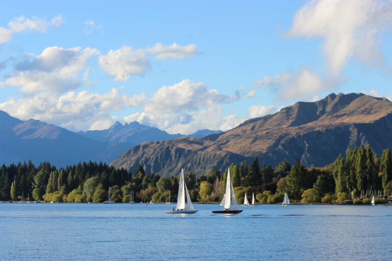 Picturesque sailboat on Lake Wānaka with a tan mountain in the background and a blue mountain behind it.