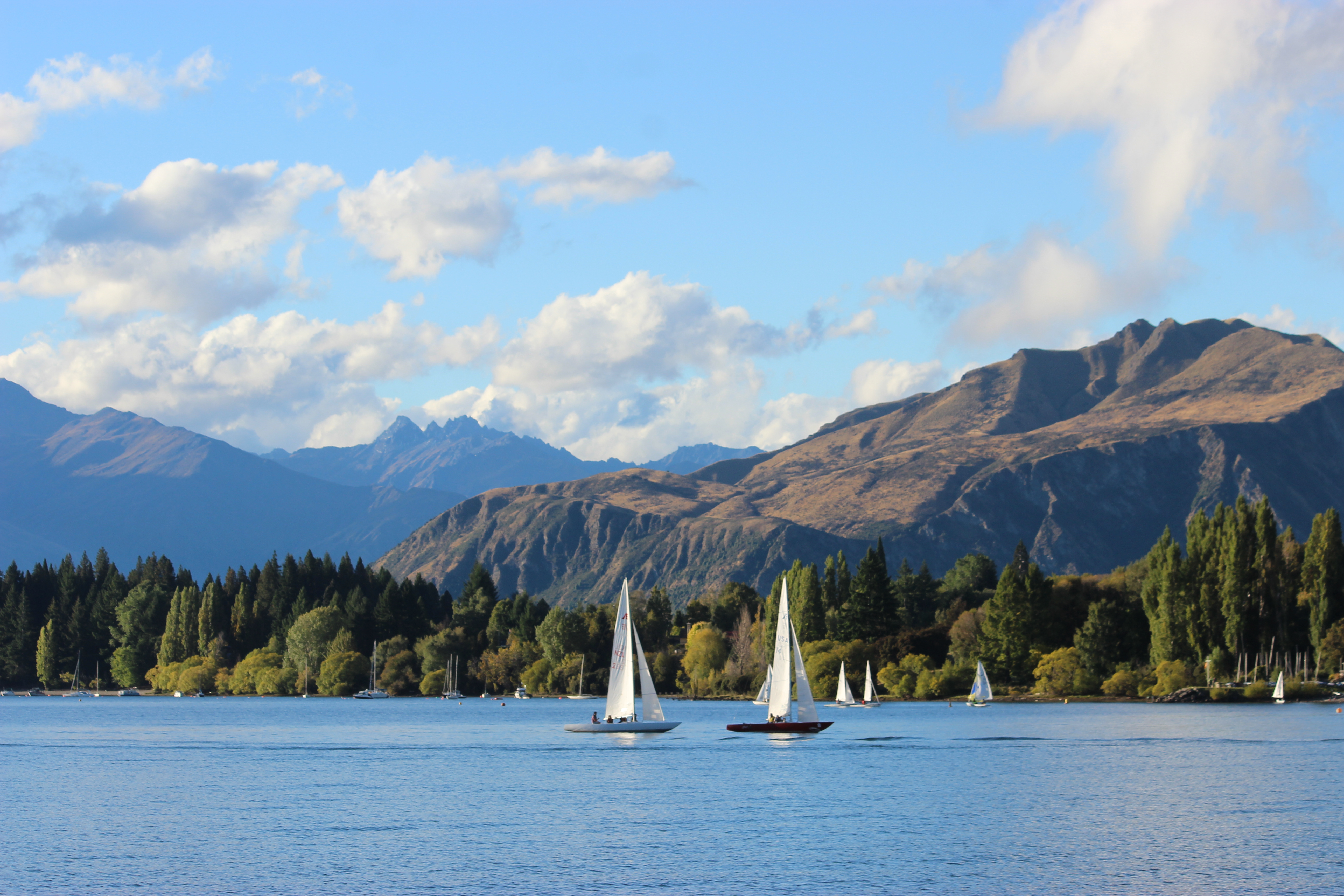Picturesque sailboat on Lake Wānaka with a tan mountain in the background and a blue mountain behind it.