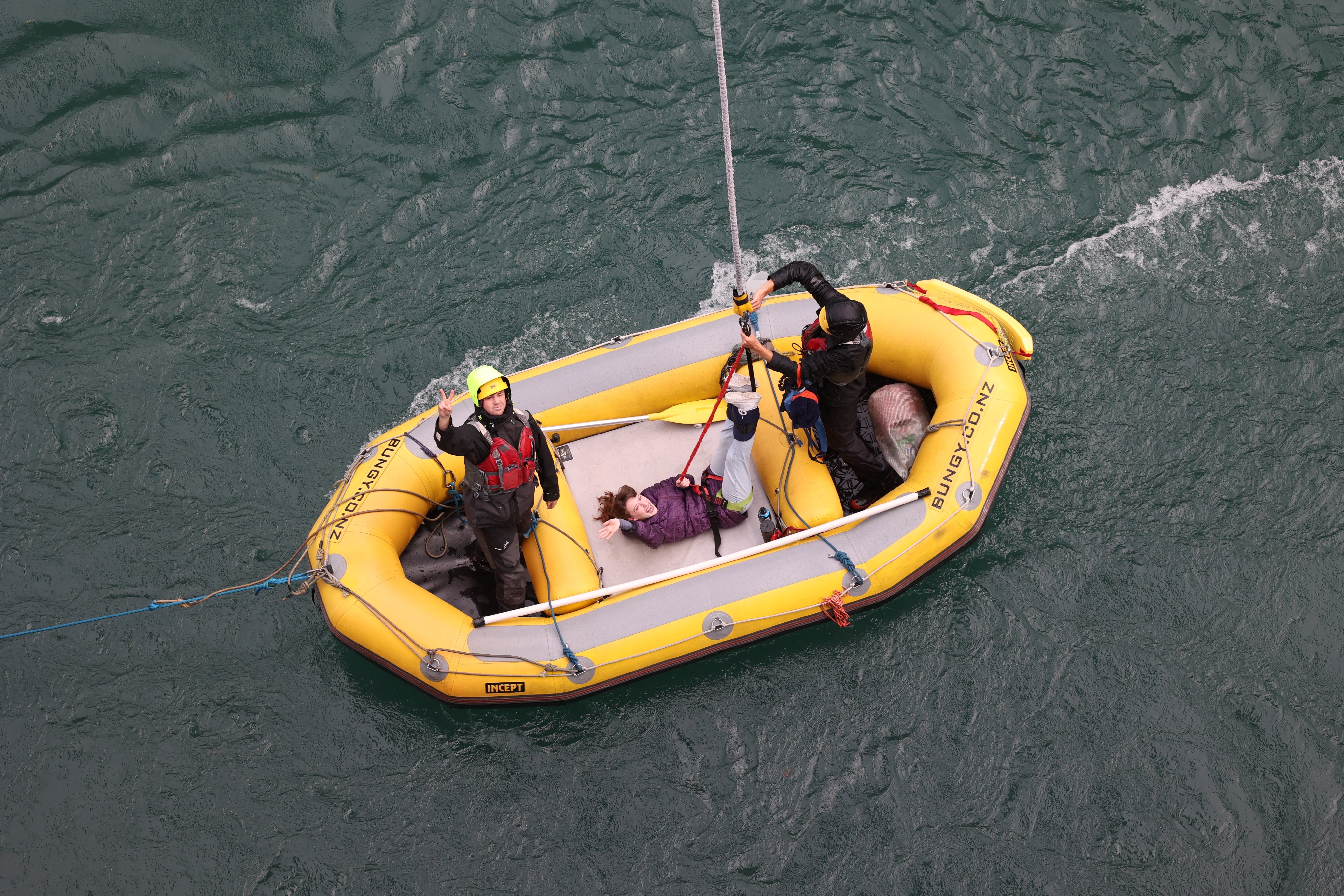 A young woman smiling and waving to the camera as she lays on the yellow collection raft after bungee jumping off Kawarau Bridge.