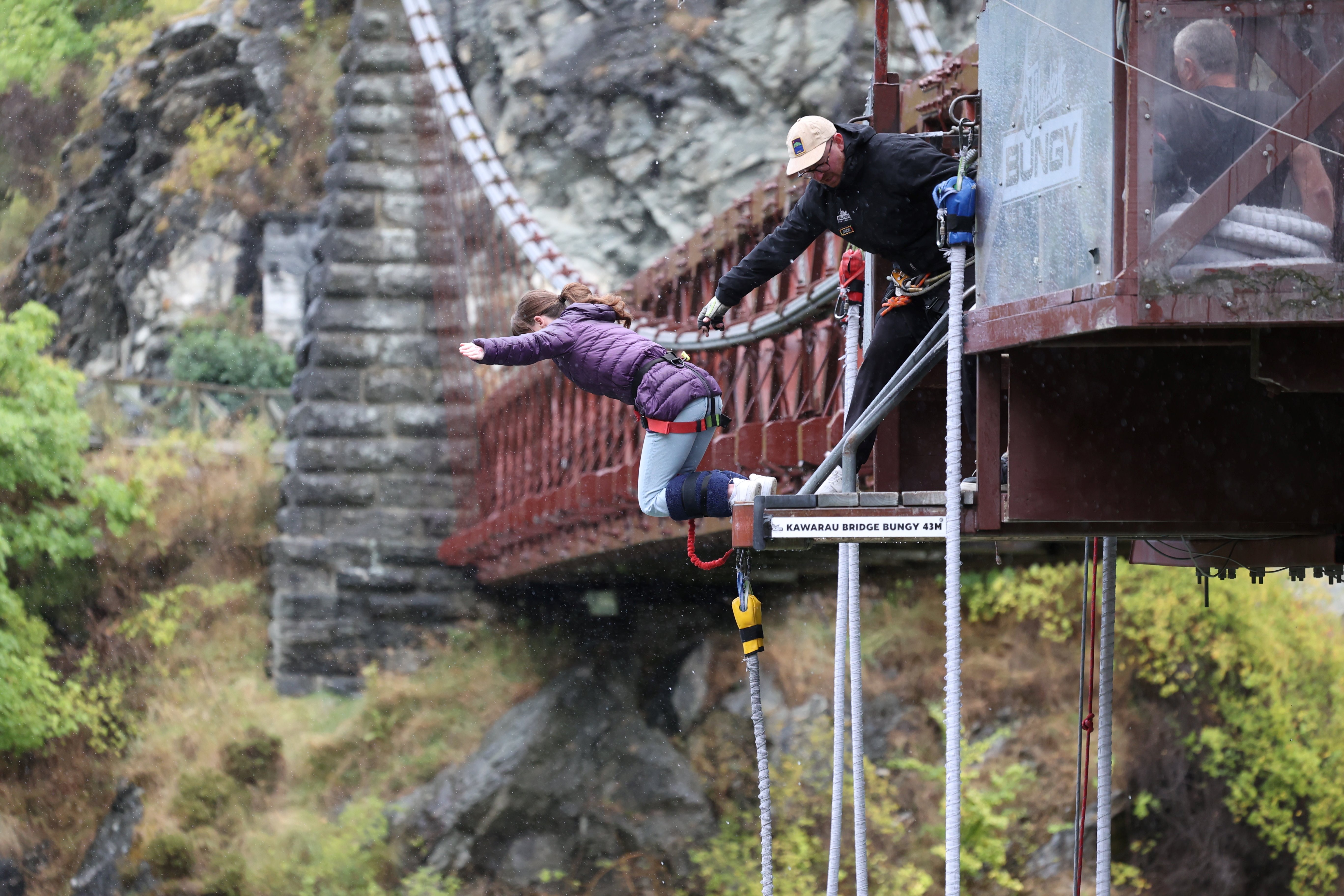A young woman carefully dropping off the bungee platform with bungee cords tied around her feet at the Kawarau Bridge.