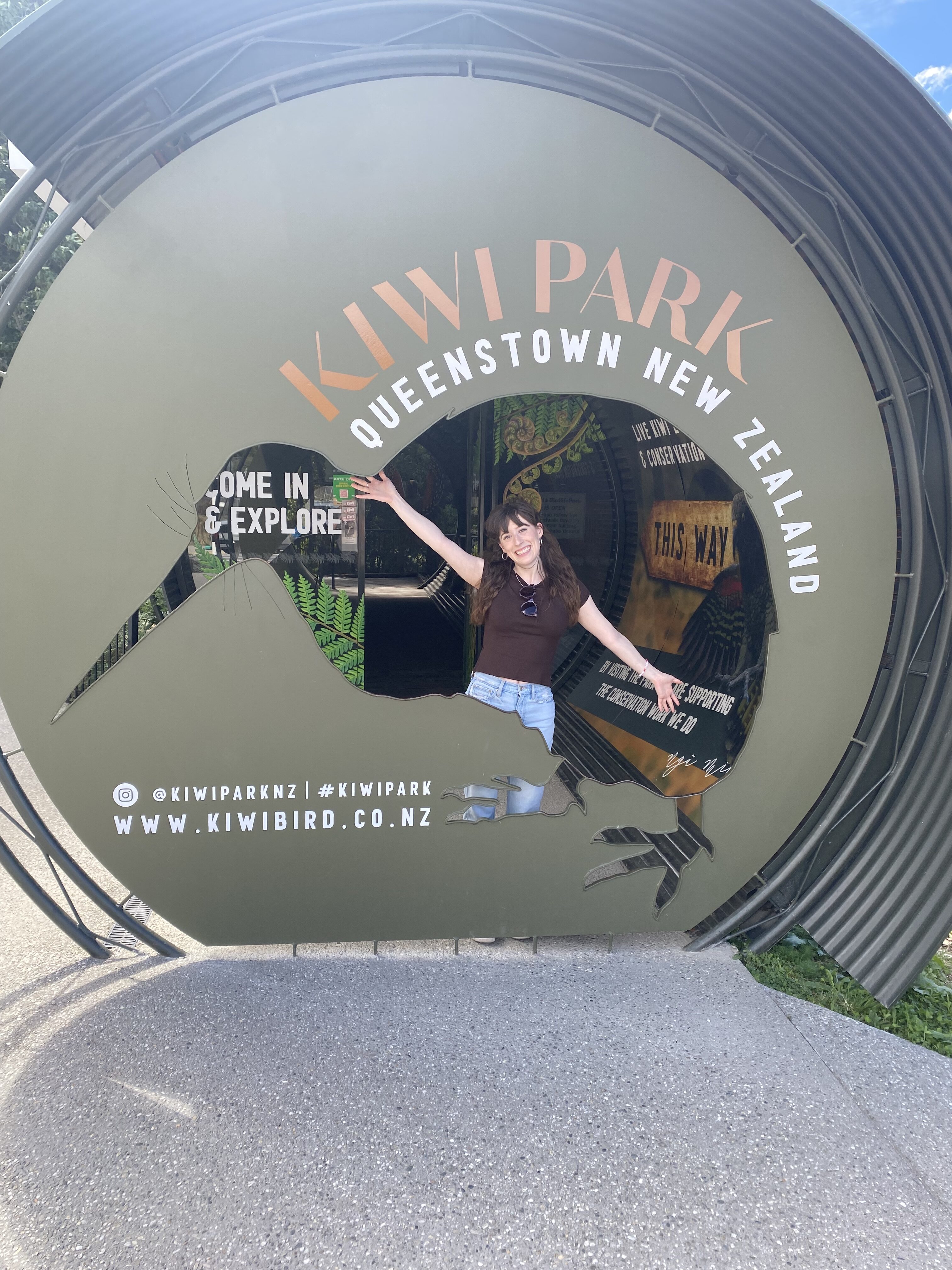 A young woman standing in front of Kiwi Park sign.