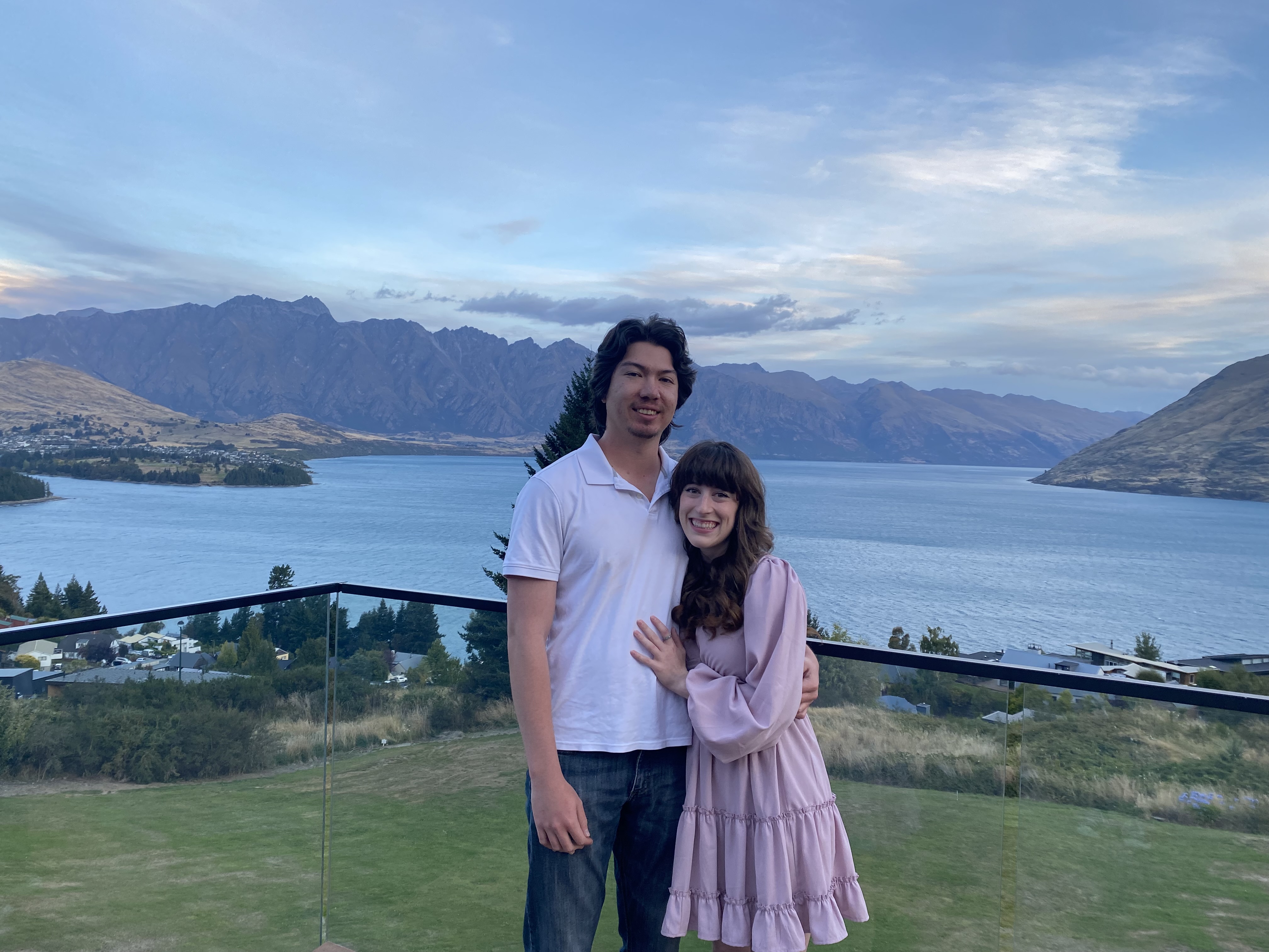 A couple smiles together on a balcony overlooking Lake Wakatipu at Kamana Nest.