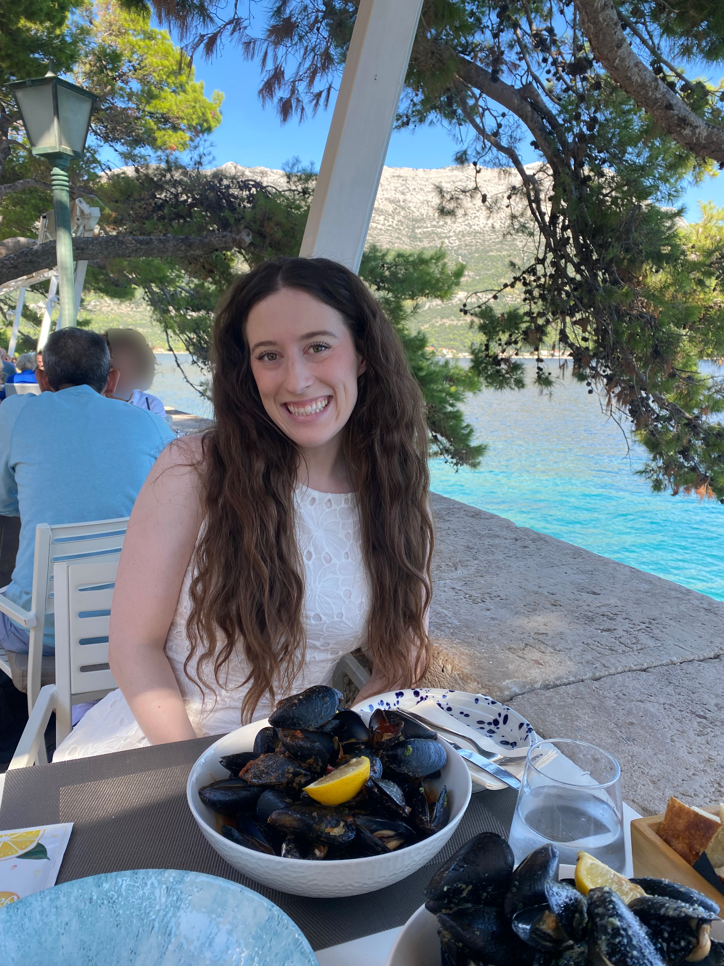 A young brunette woman smiling with a plate of fresh mussels – Korčula Old Town.
