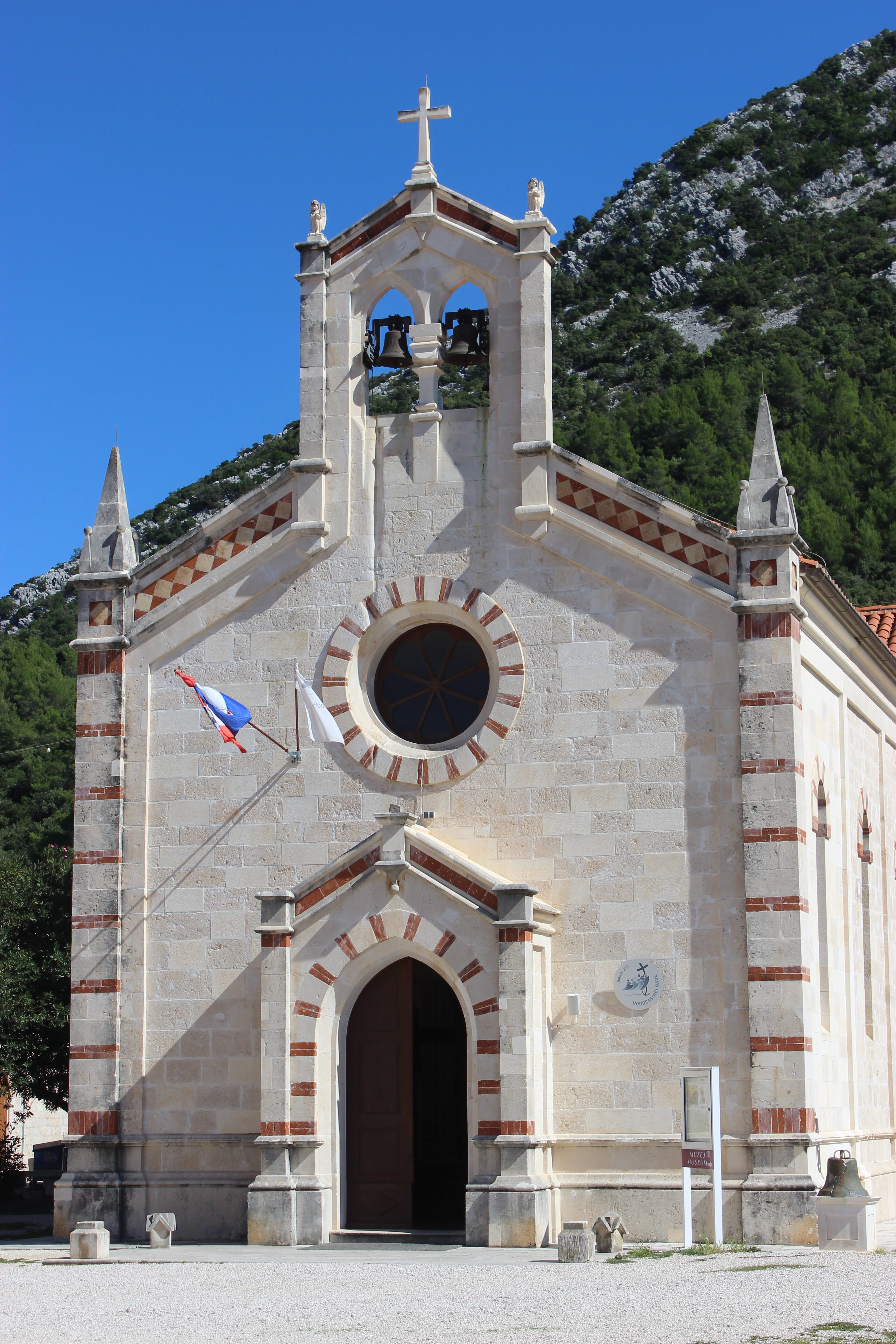 A cream-colored stone church in Ston, Croatia with a beautiful archway and a circular window.