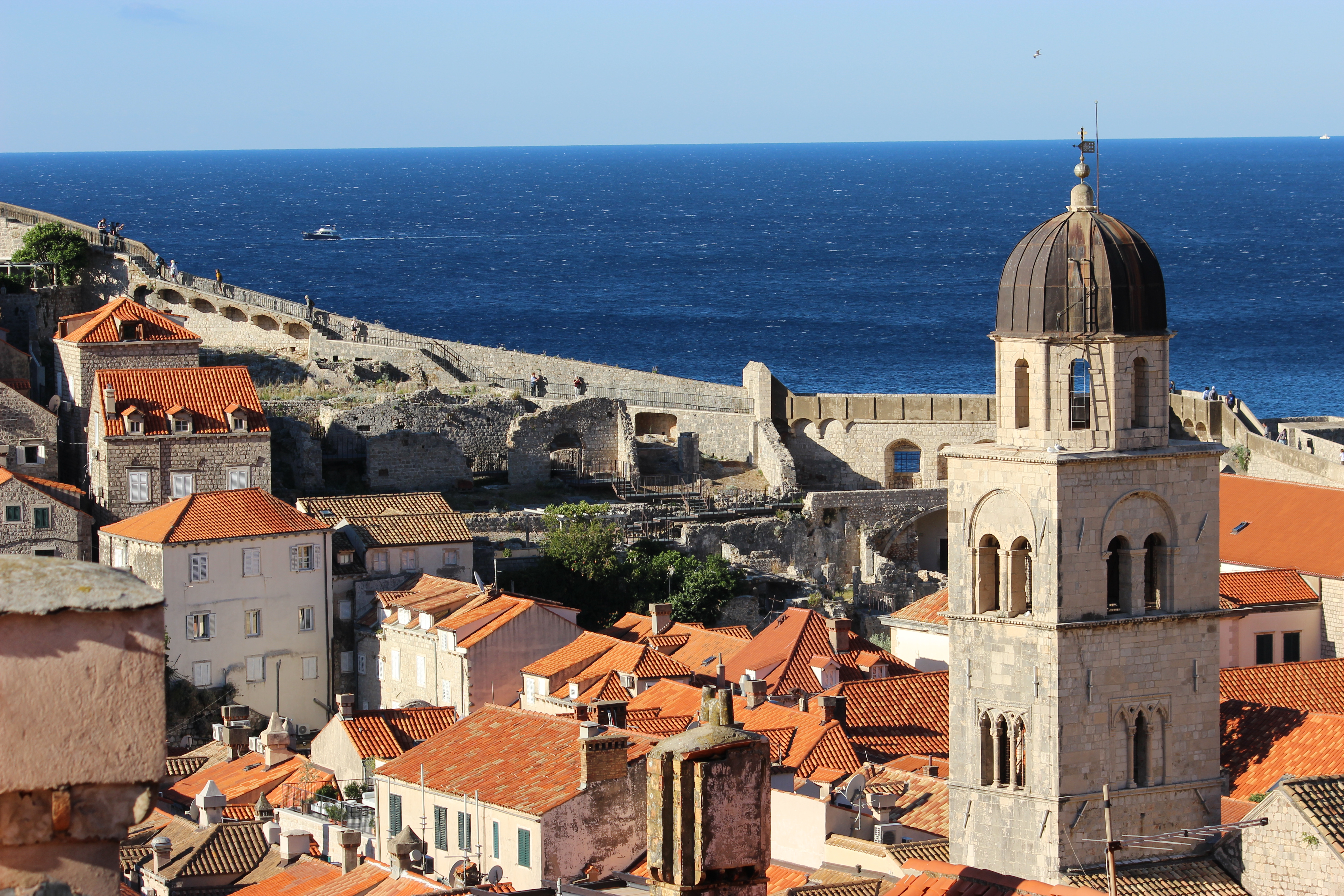A bell tower in Dubrovnik framed by orange roofs and the dark blue Adriatic Sea.