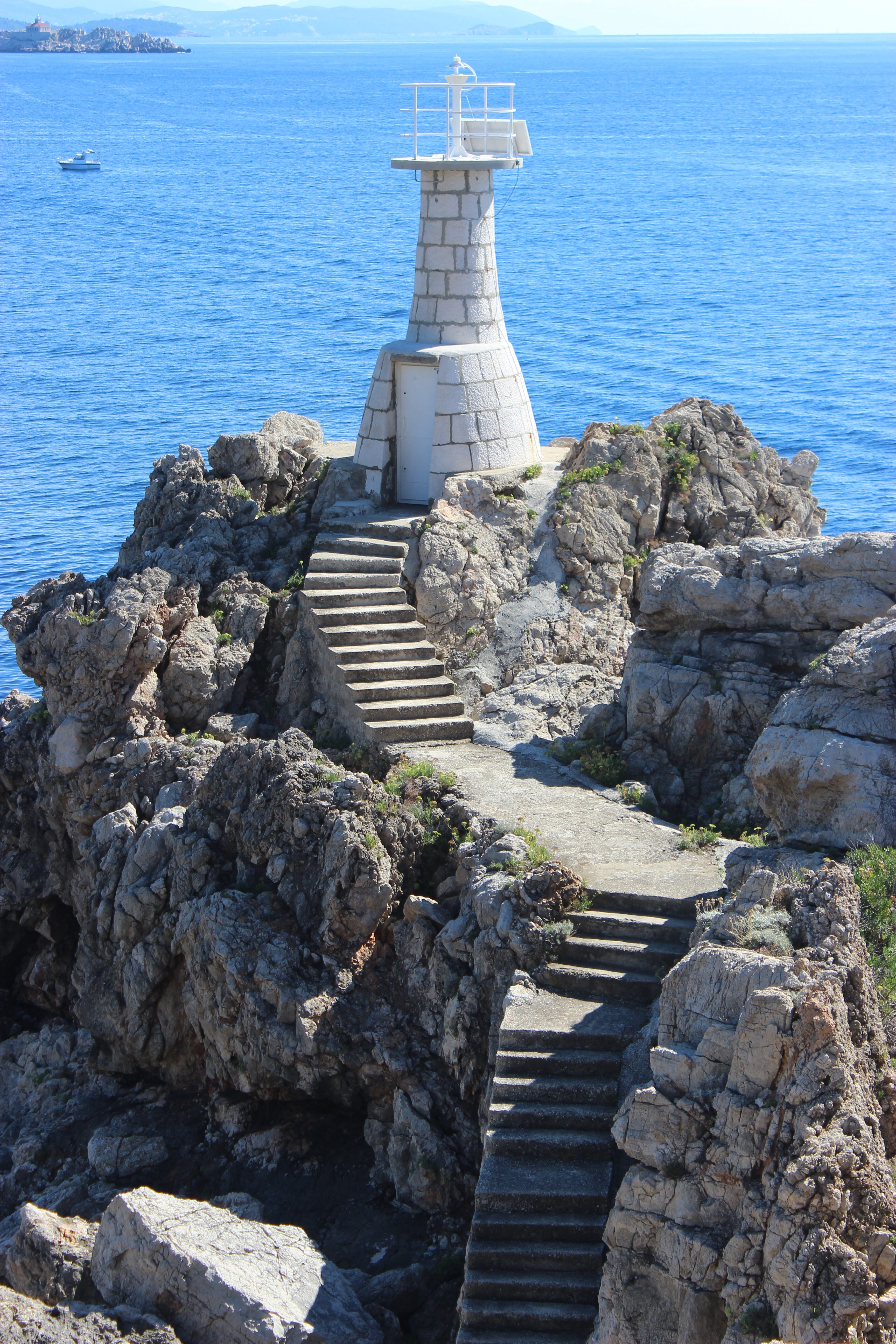 A white stone lighthouse above concrete steps surrounded by jagged rocks on Koločep (Elaphiti).