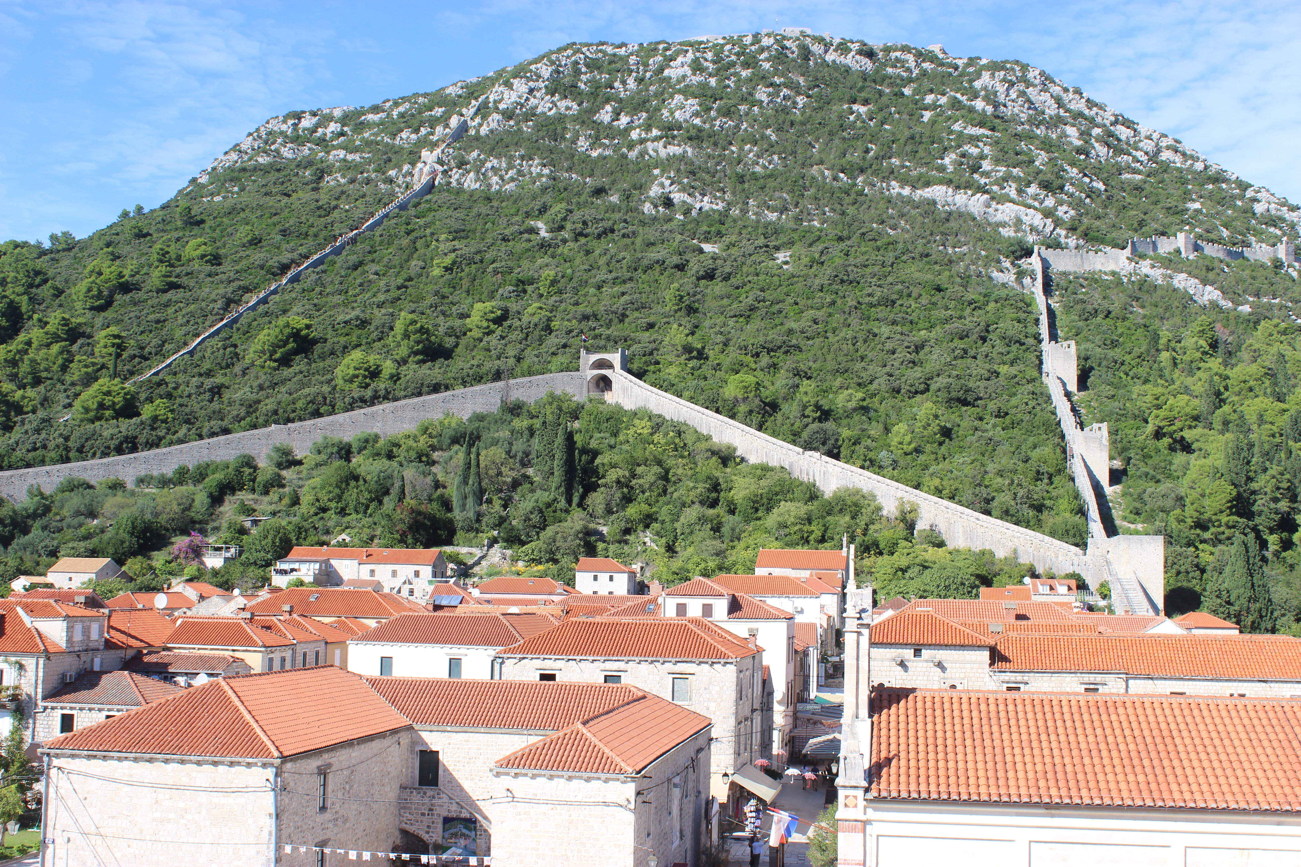 The historic orange-roofed village of Ston with the monumental Ston Wall climbing the green hillside.