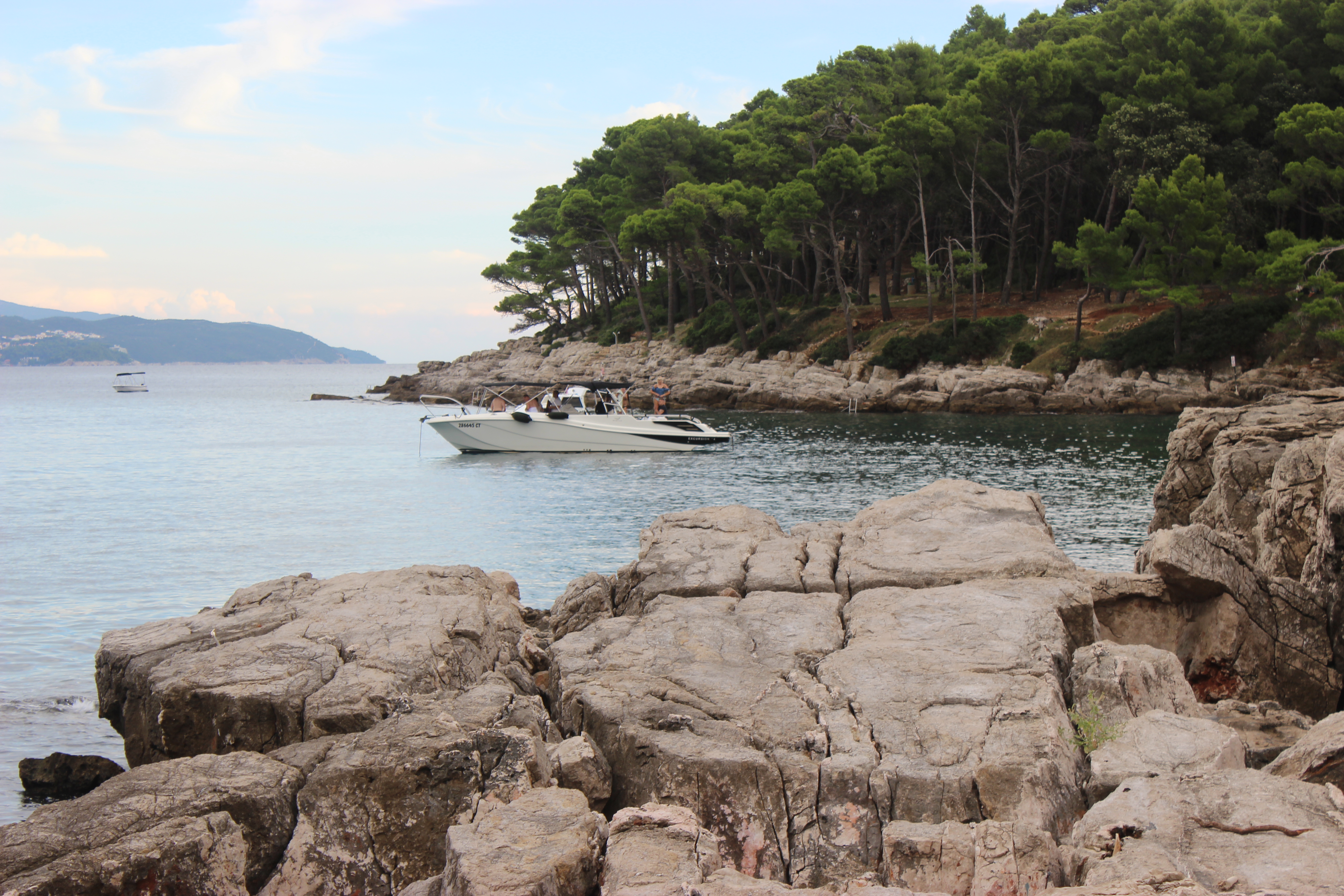 The rocky shoreline of Lokrum Island with a boat docked along the rocks.