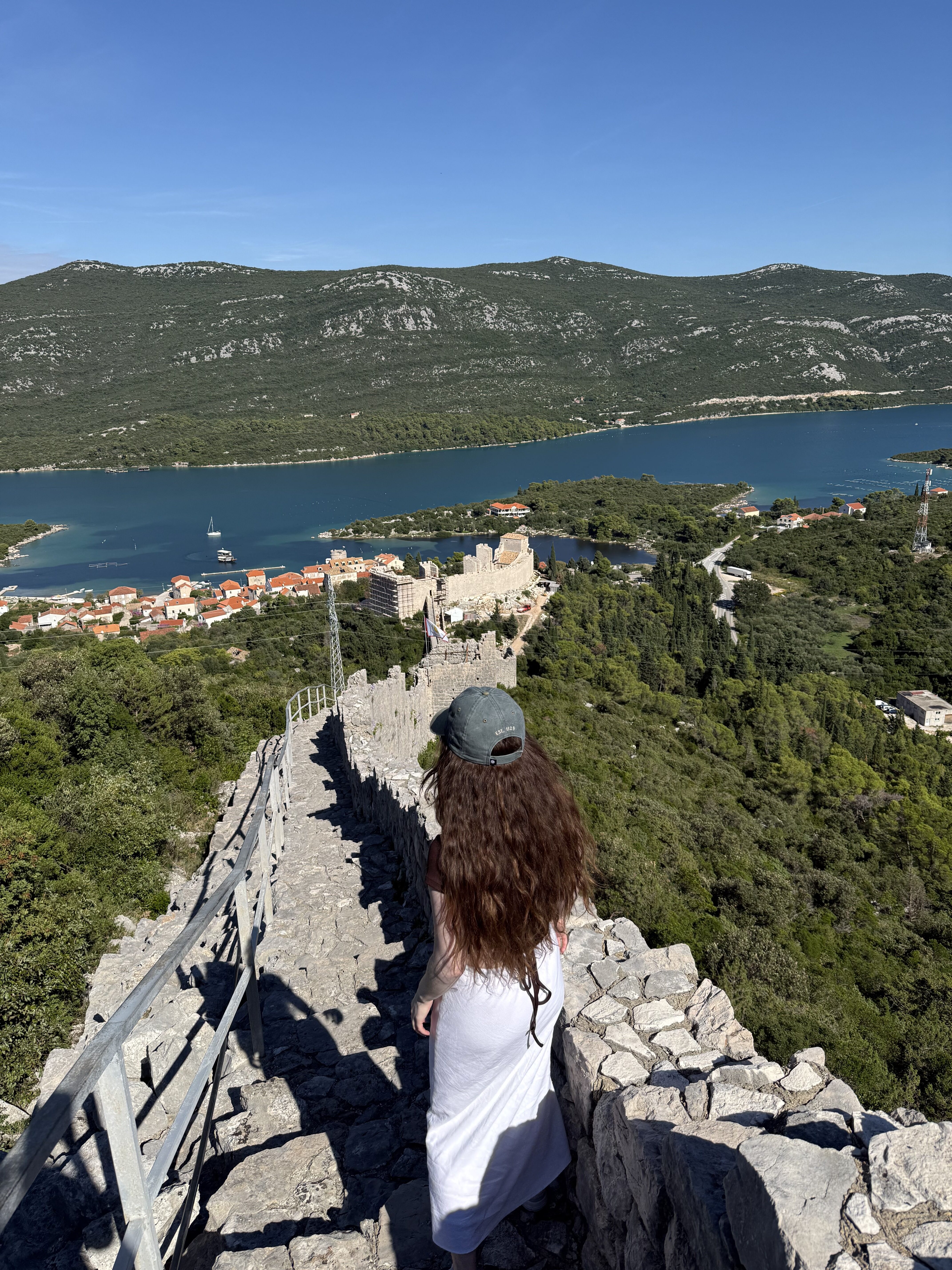 A young woman with brunette hair gazing out upon Mali Ston from the Ston Walls.