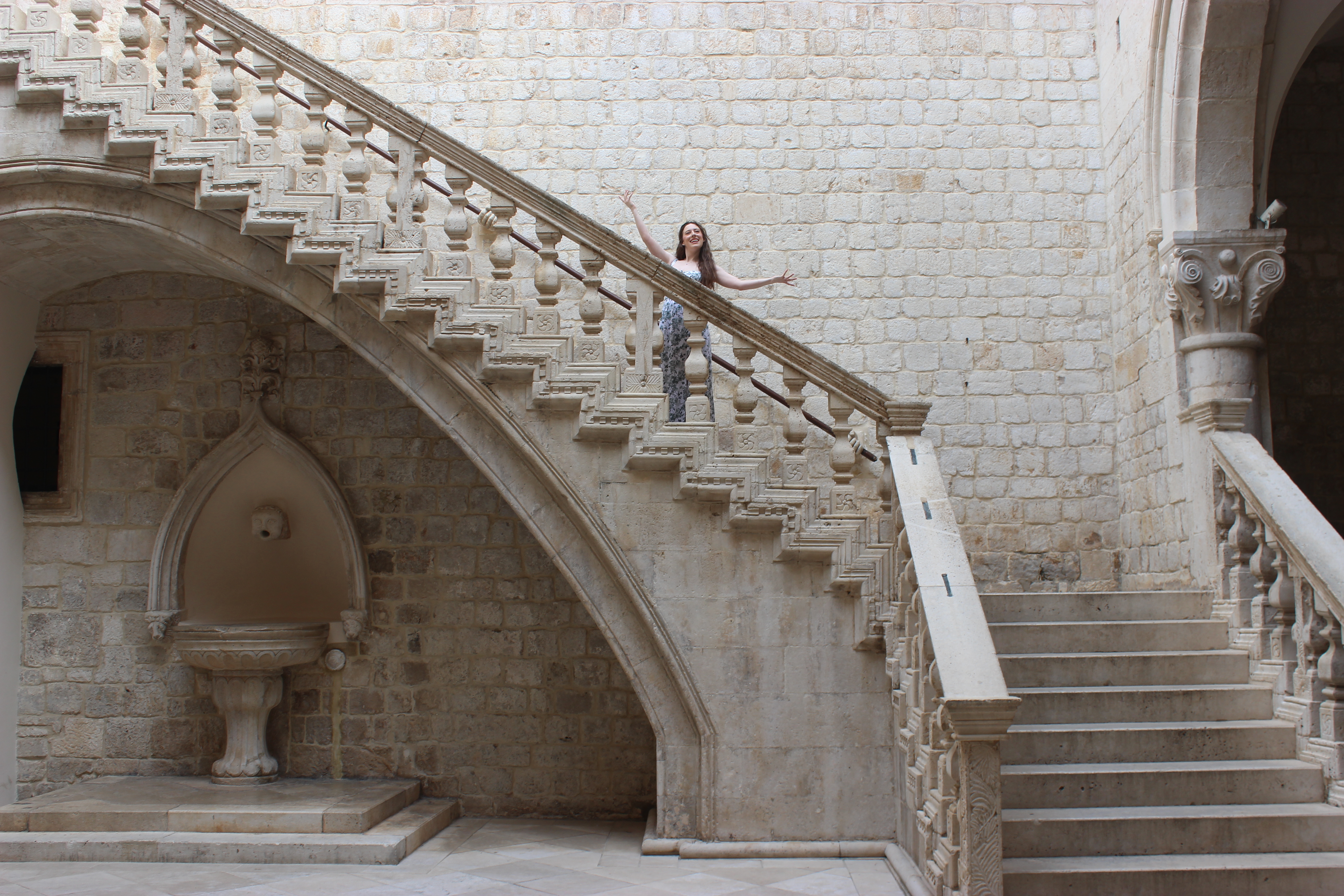 A young woman posing on a beautiful cream-colored stone staircase in Rector's Palace.