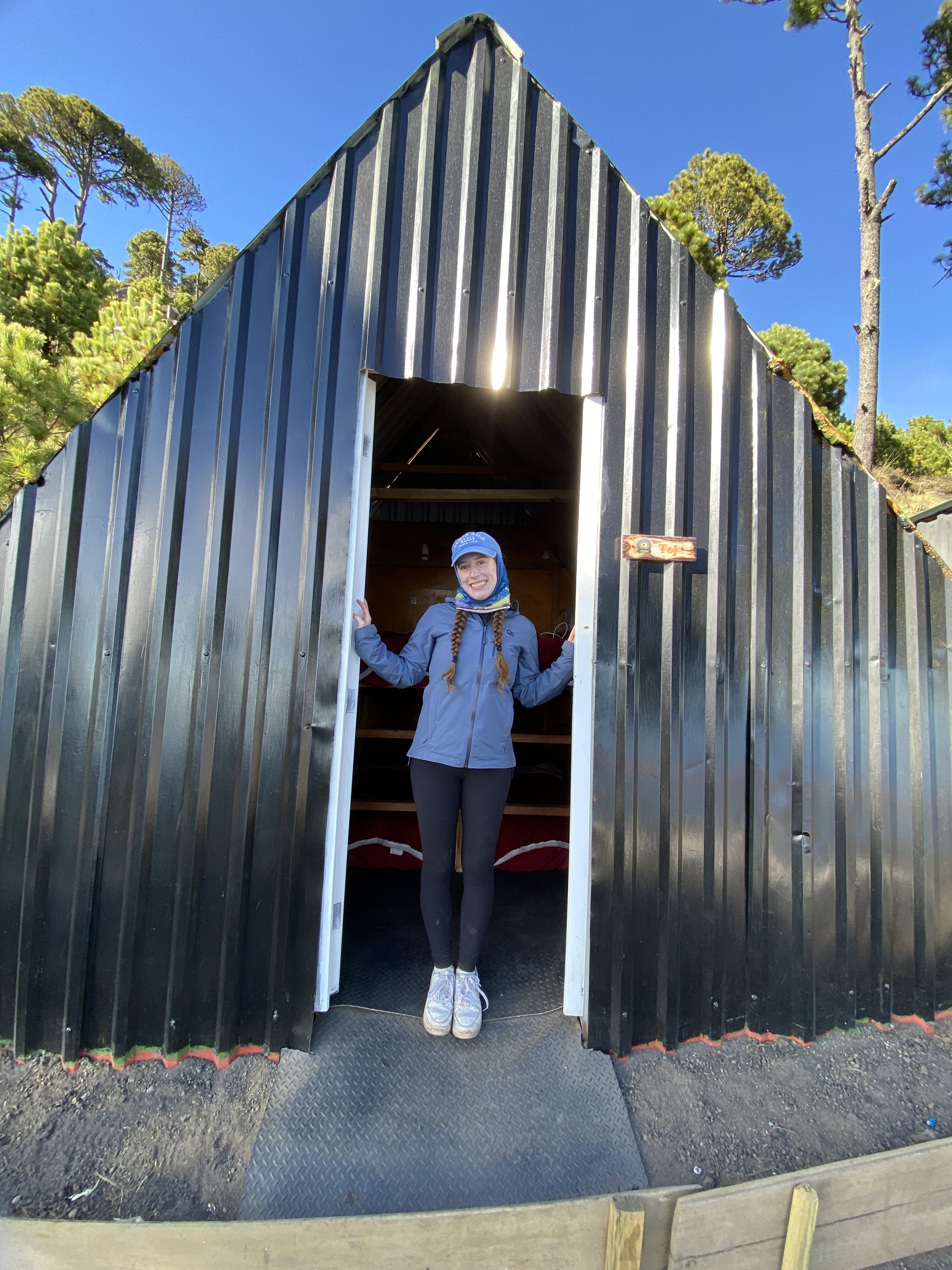 Bella smiling in the doorway of an A-frame cabin at Wicho and Charlie's Acatenango base camp.