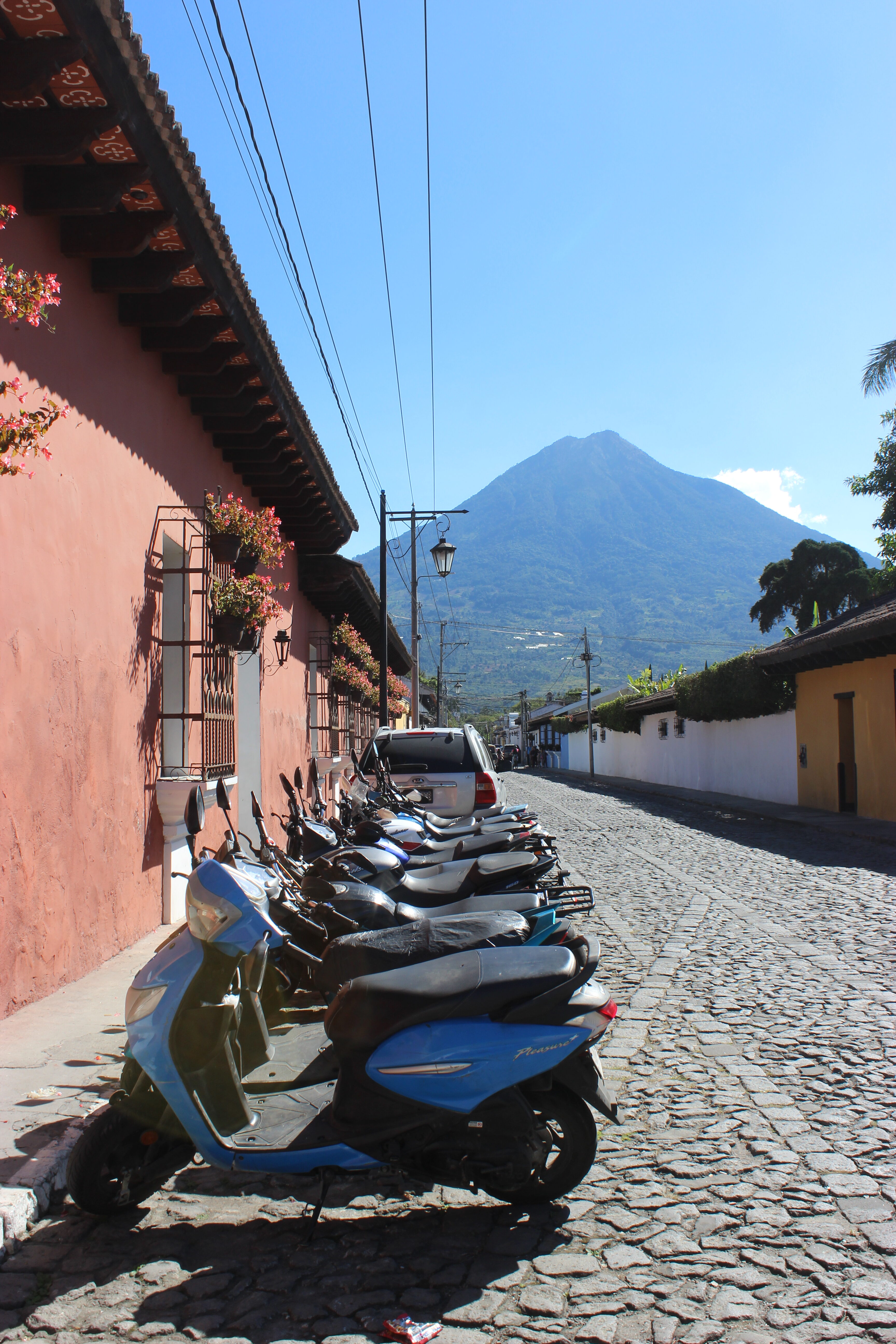 Cobblestone street in Antigua, Guatemala with motorbikes and Agua Volcano in the background.