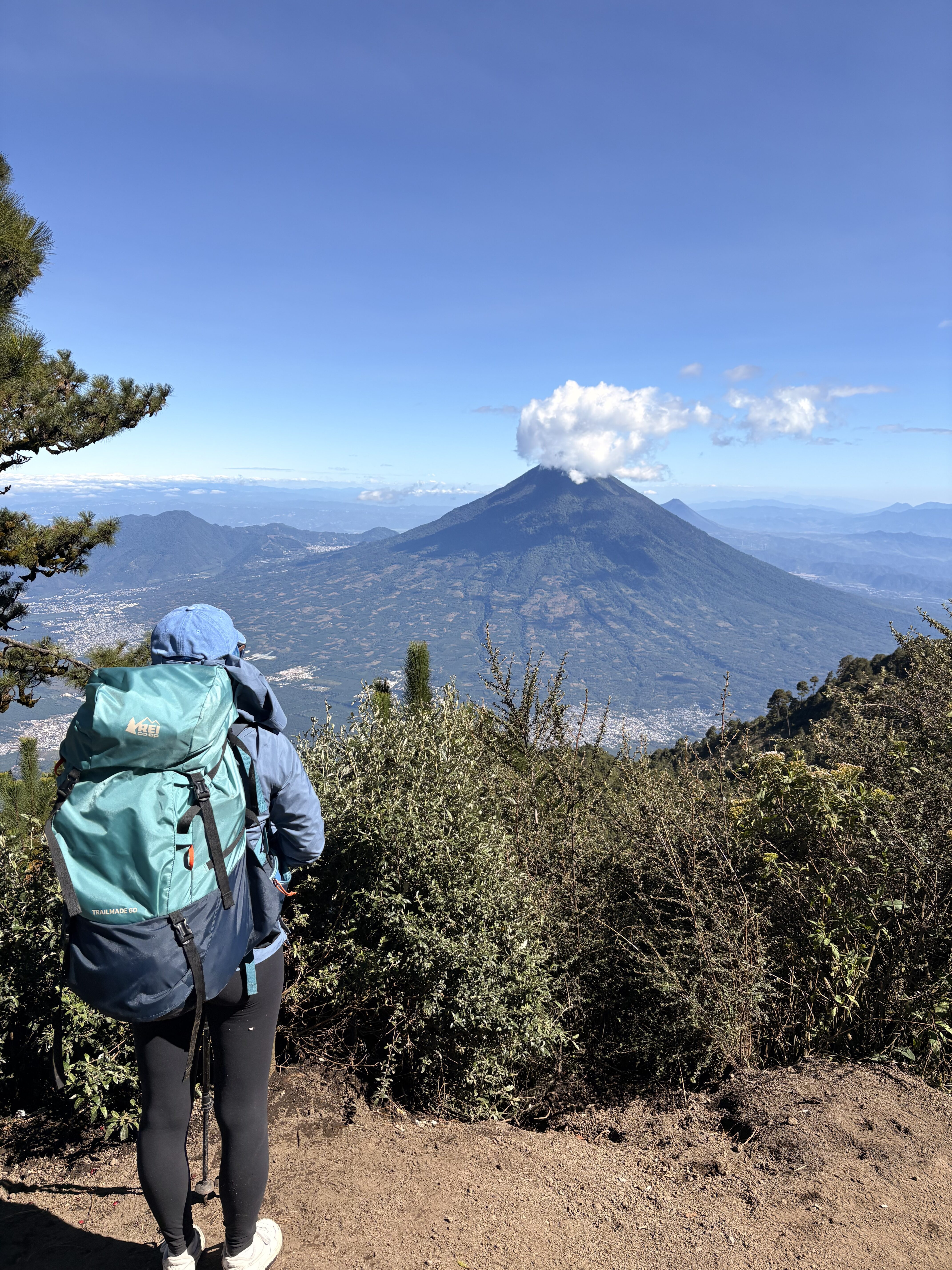 Backpacker with a teal backpack looking out upon a volcano in Guatemala from the Acatenango Volcano hiking trail.