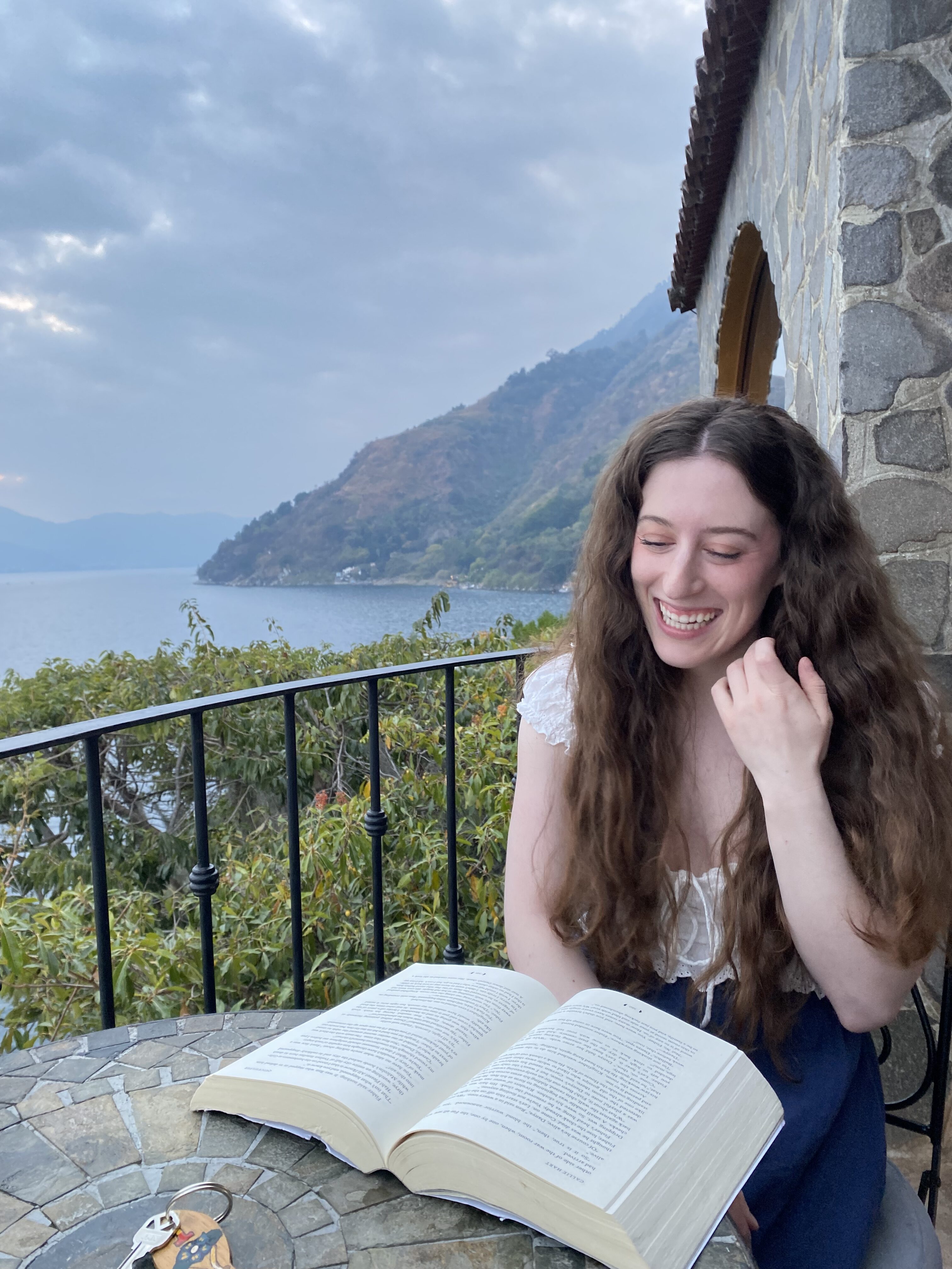 Bella, reading on a balcony at La Casa del Mundo with Lake Atitlán in the background.