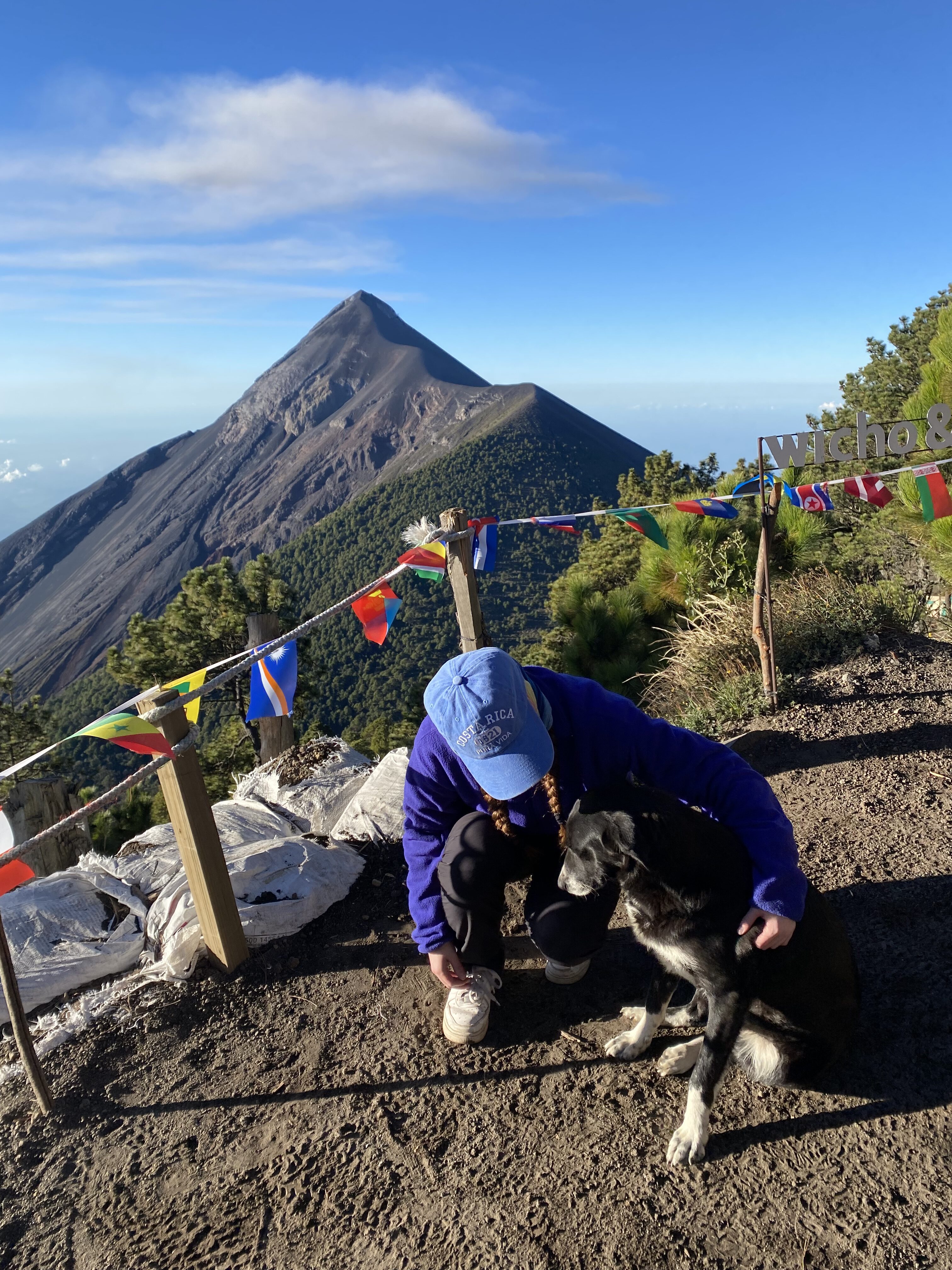 A young crouched beside a black dog at Acatenango base camp with Fuego in the background.