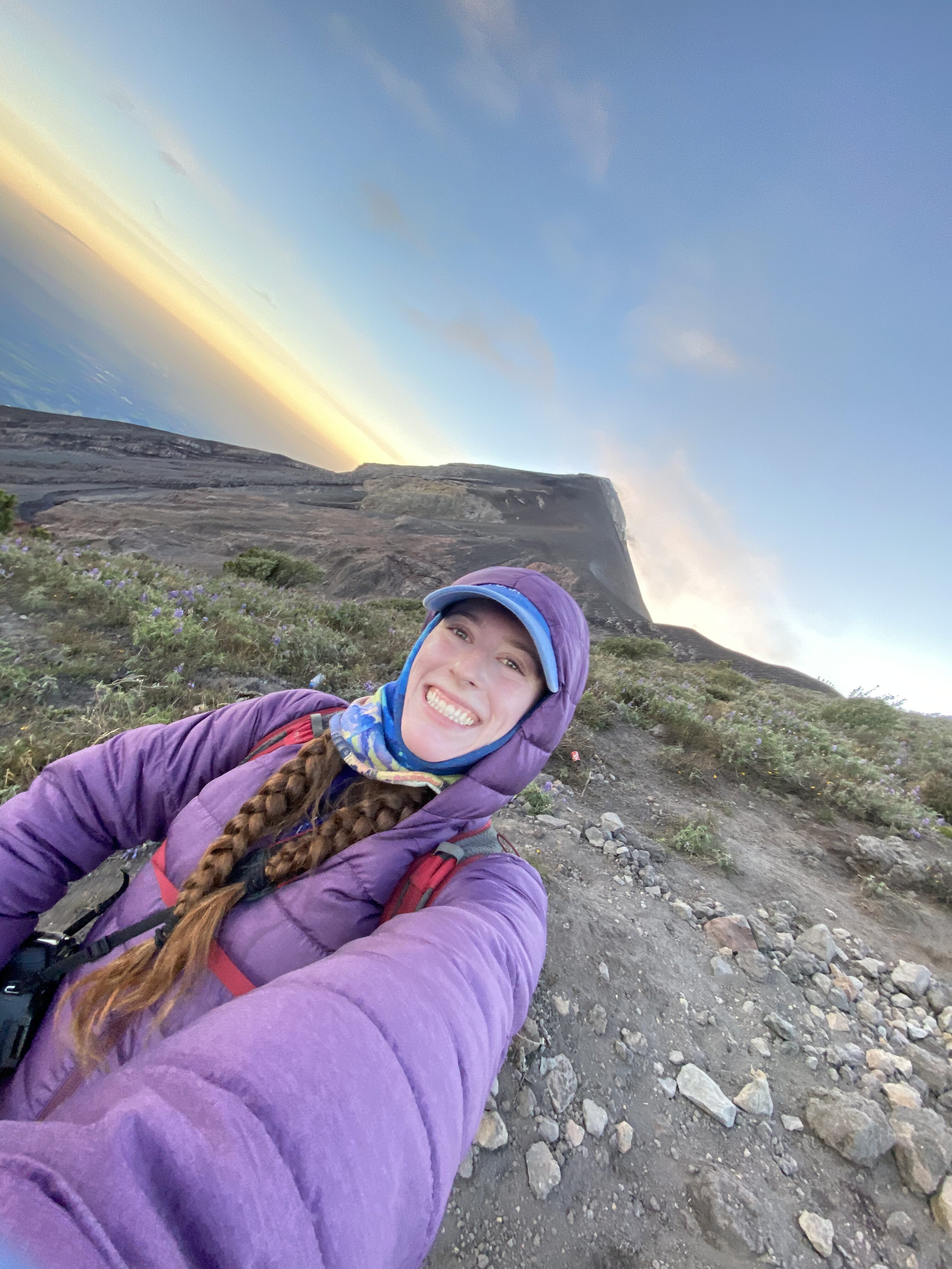 Bella smiling from the open ridge on Fuego volcano with the active volcano in the background.