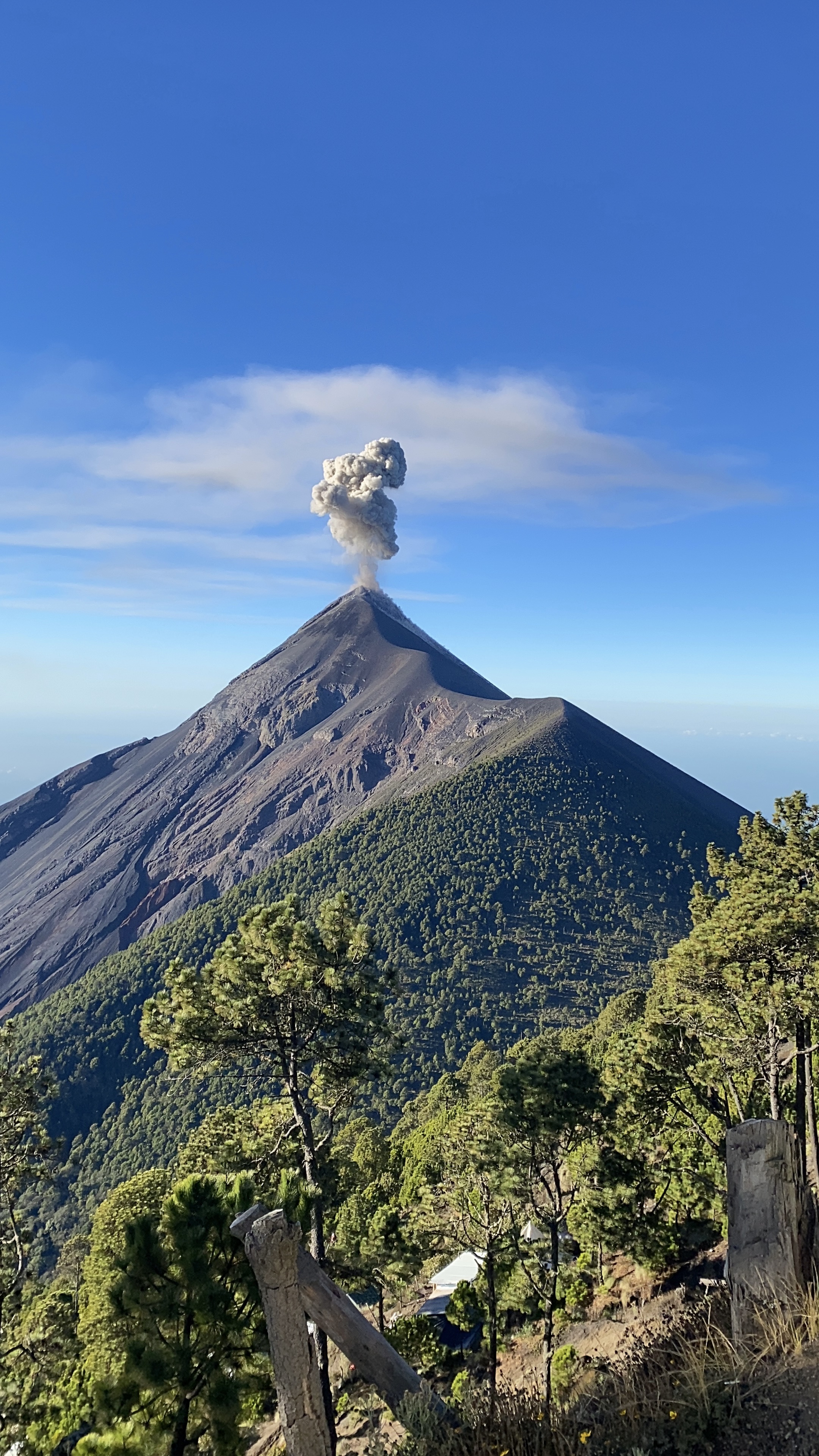 Fuego Volcano in Guatemala with a plume of silver smoke in front of a blue sky.
