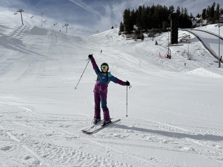 A skier wearing at three-toned (blue, turquoise and purple) ski suit posing on skis in front of Howelsen Hill ski area at Steamboat Springs, Colorado.
