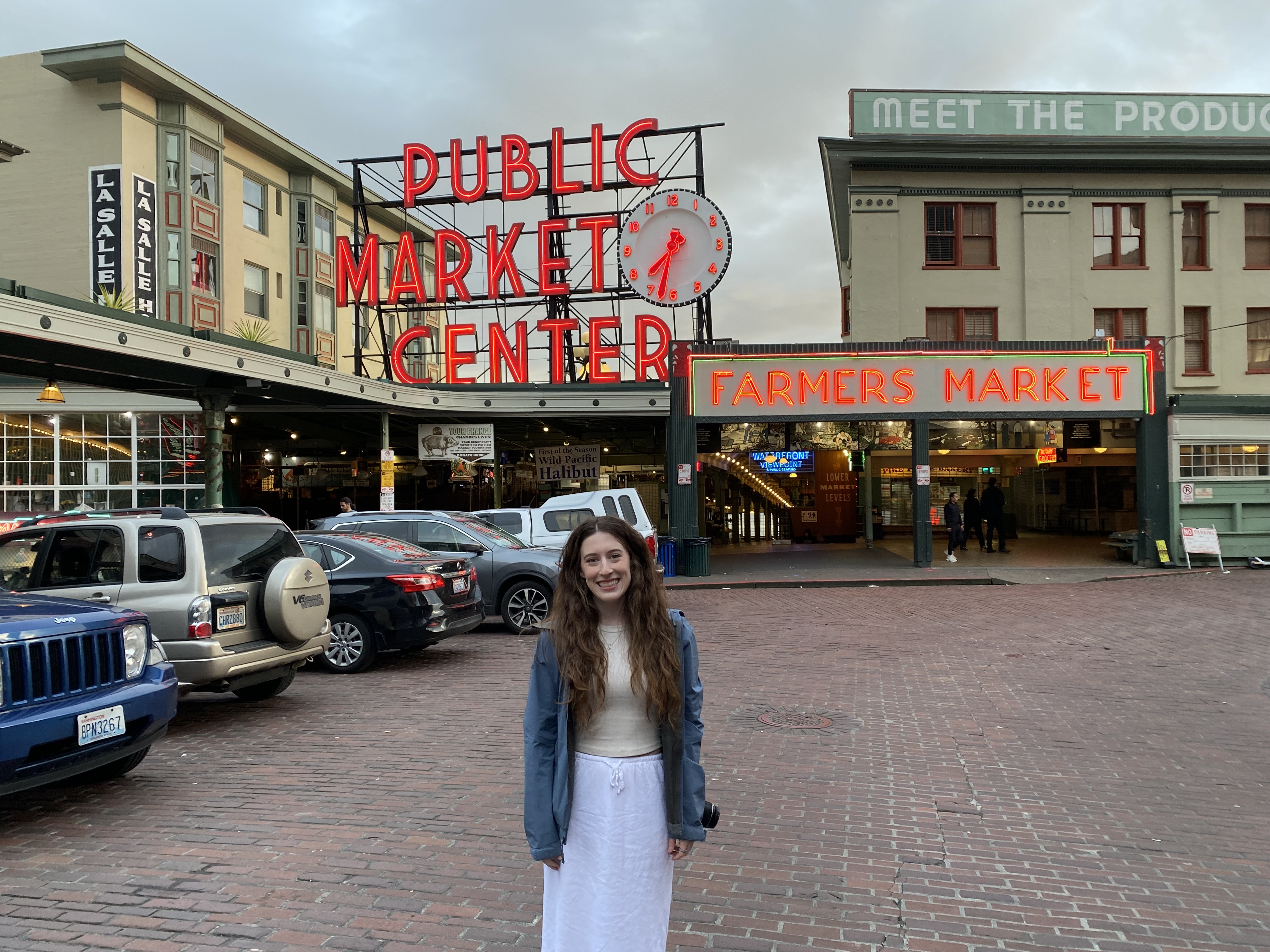 Bella smiling in front of the Pike Place Market sign which says, "Public Market Center".