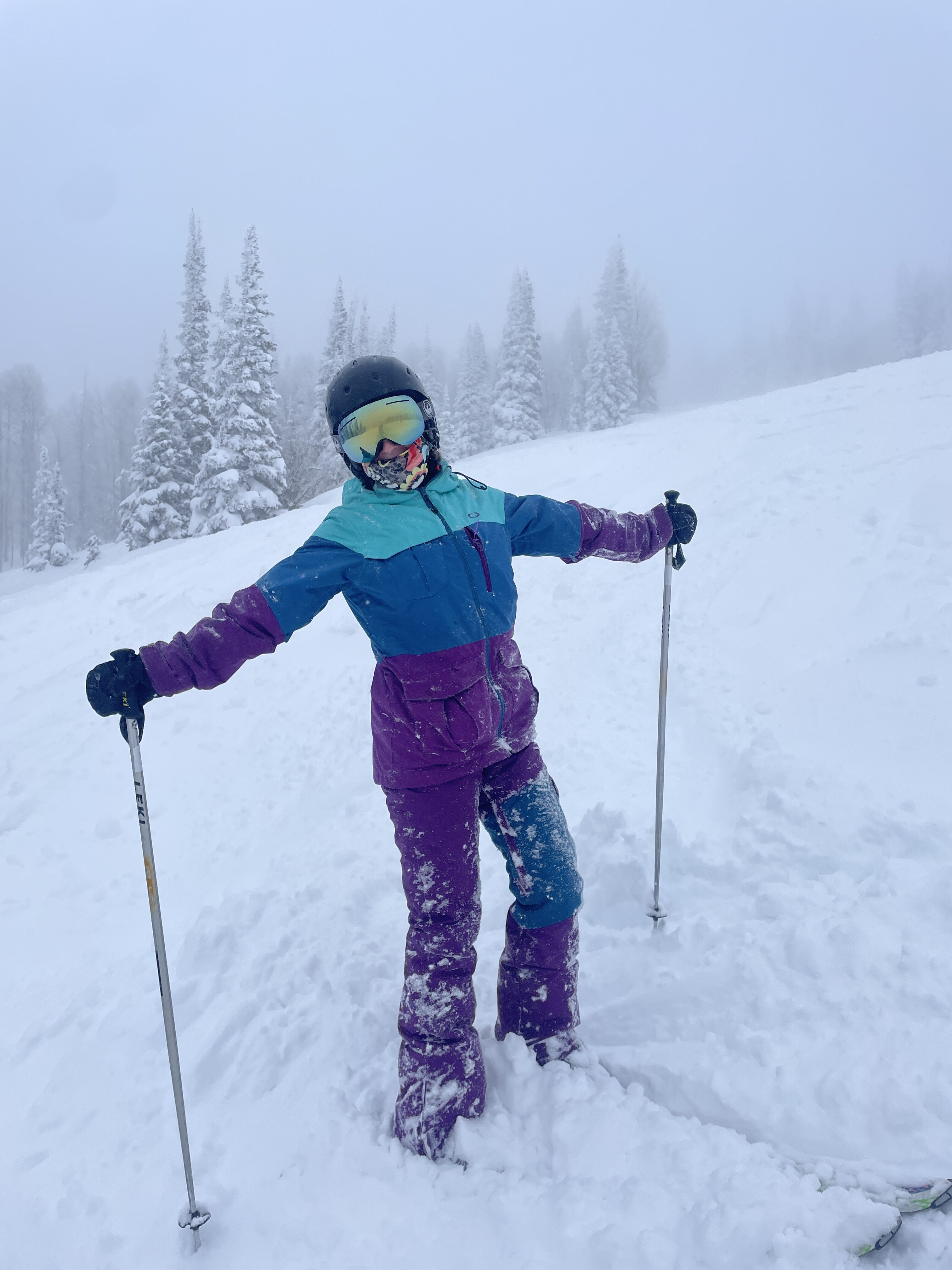 A skier with a three-toned ski suit (turquoise, blue, purple) posing with her skis buried in Steamboat's "champagne powder".