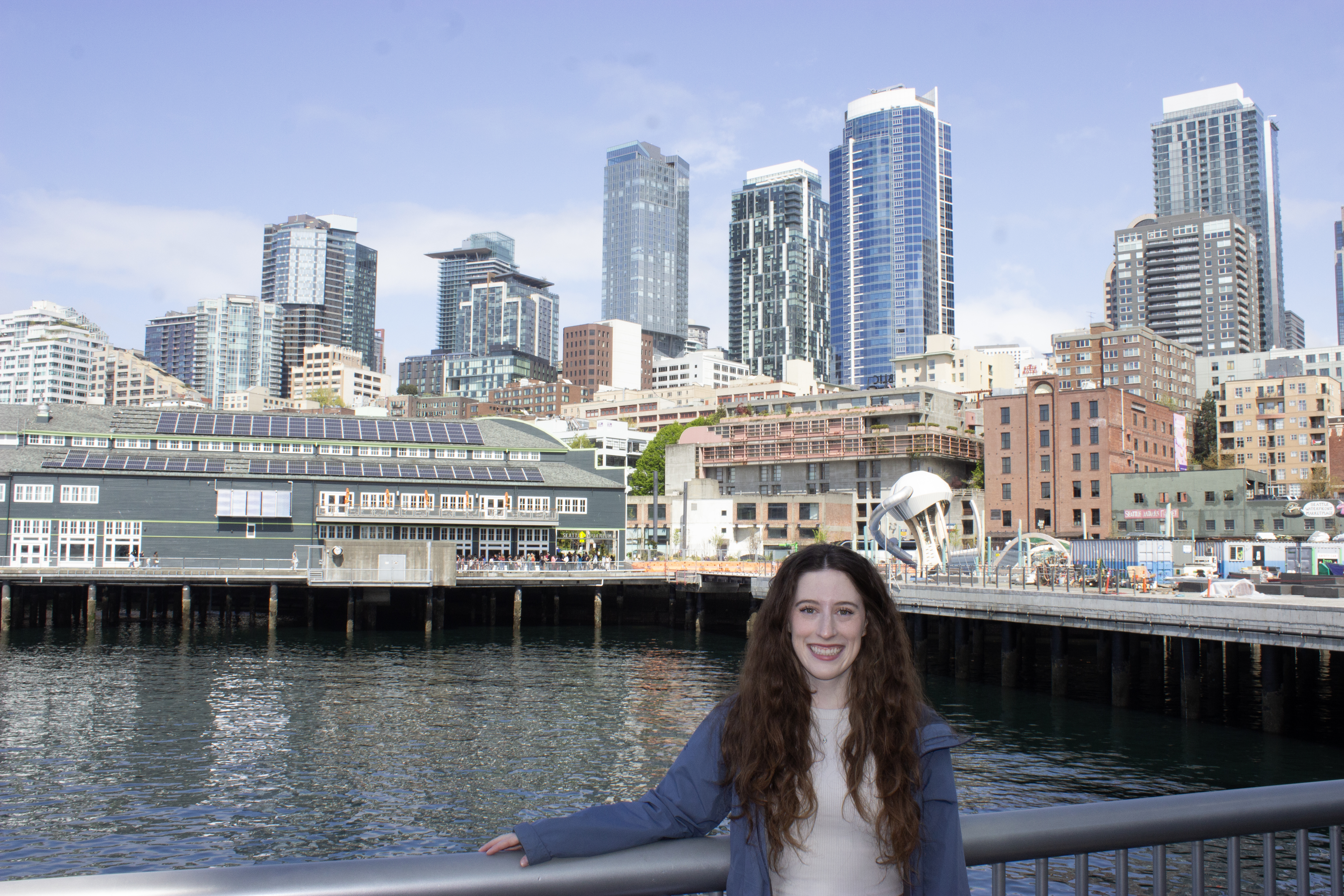 Bella smiling on a pier in Seattle with the skyline in the background.