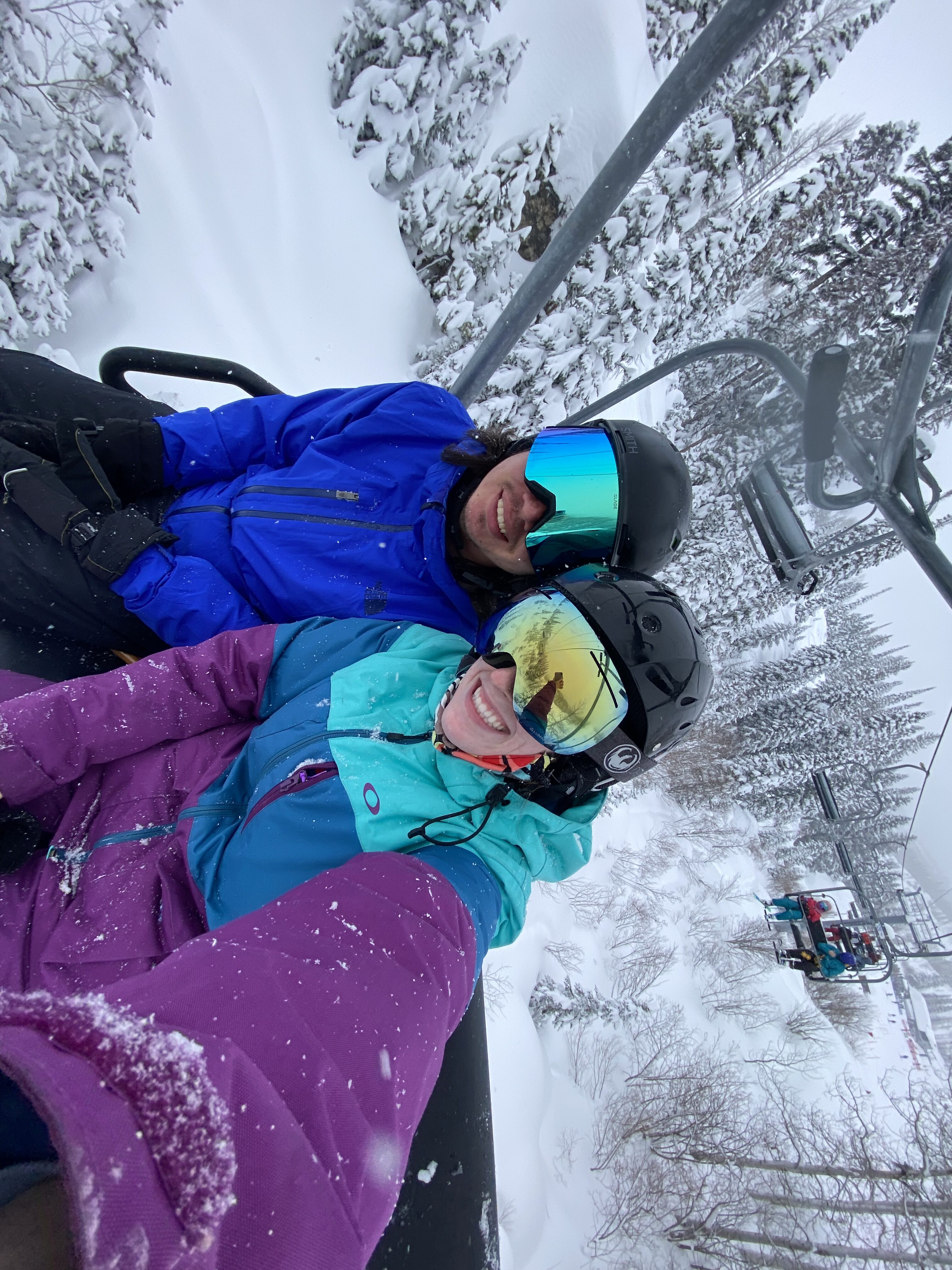 Skiers with vibrant jackets and reflective goggles, chairlift selfie.