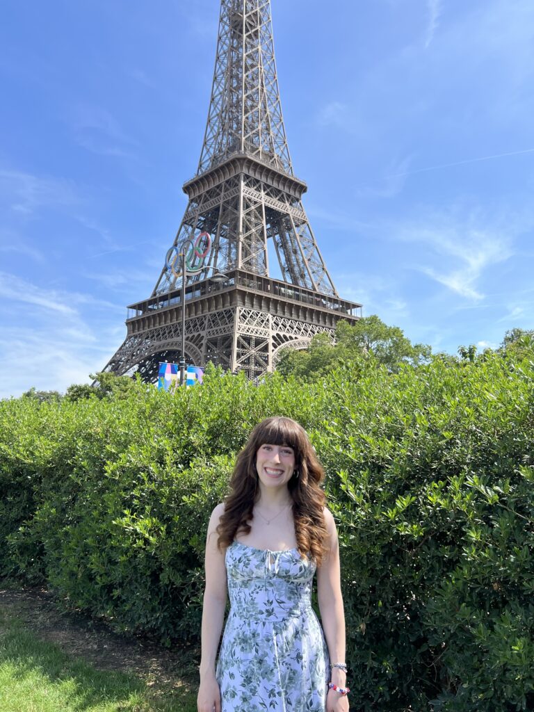 Bella smiling in front of the Eiffel Tower with the Olympic rings on the front.