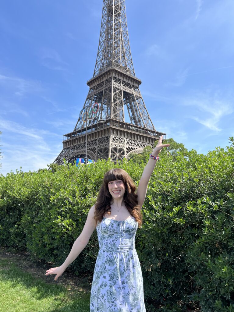 Bella posing in a green floral dress with the Eiffel Tower with the Olympic rings (2024 Paris Olympics).