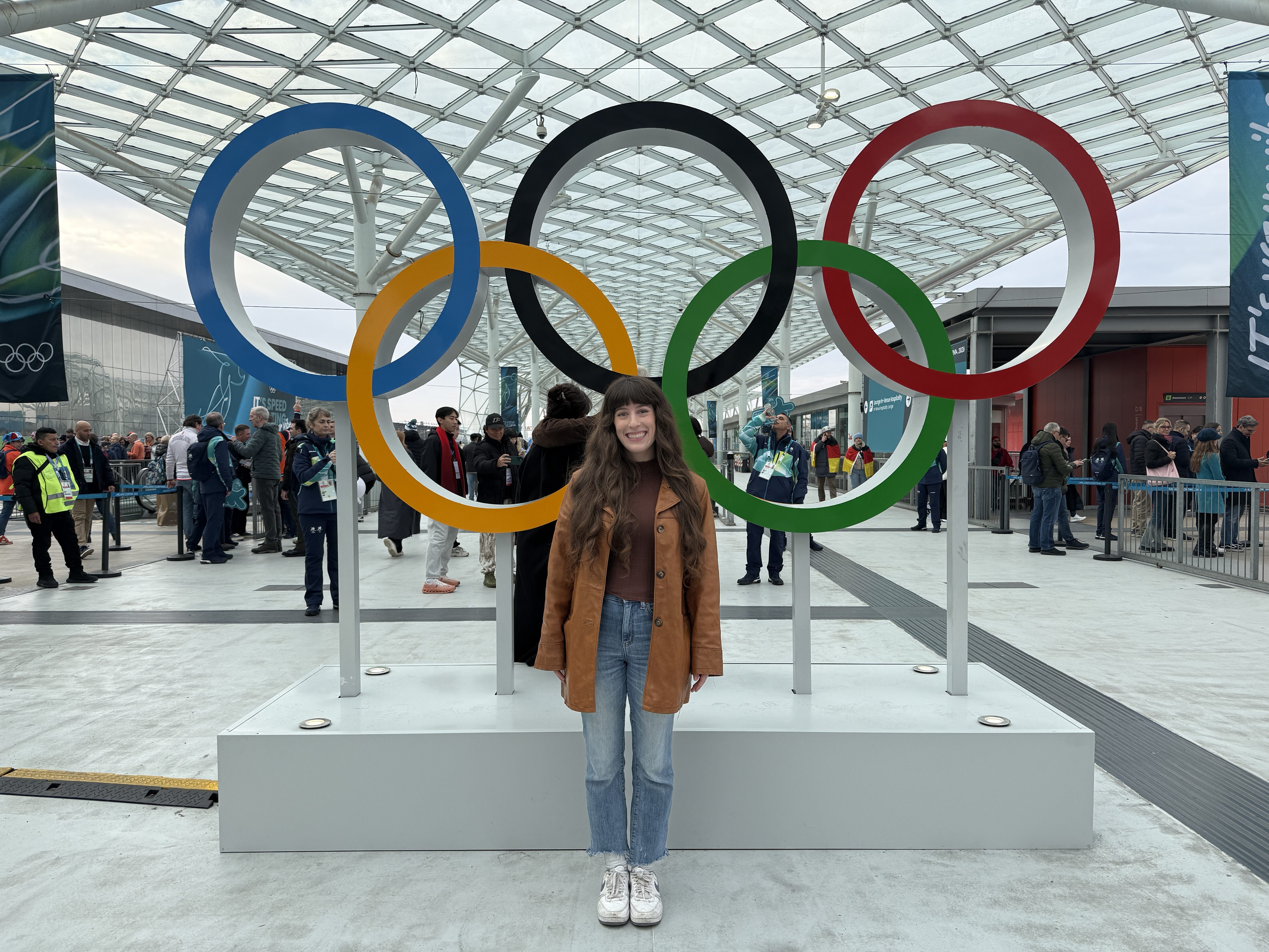 Bella smiling in front of the Olympics rings at the 2026 Milano-Cortina Olympics.