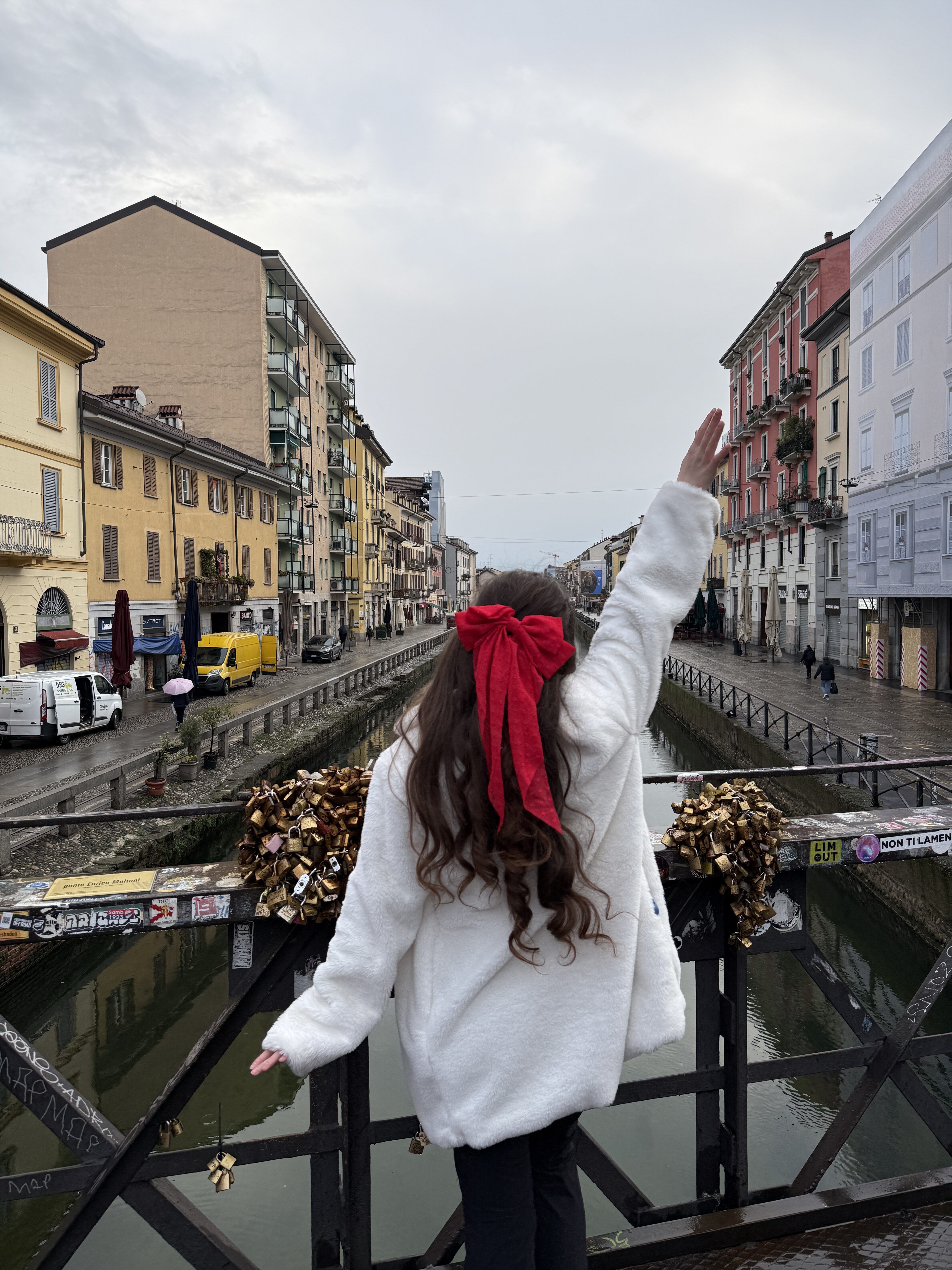 Bella posing in Navigli with a red bow and a white coat.