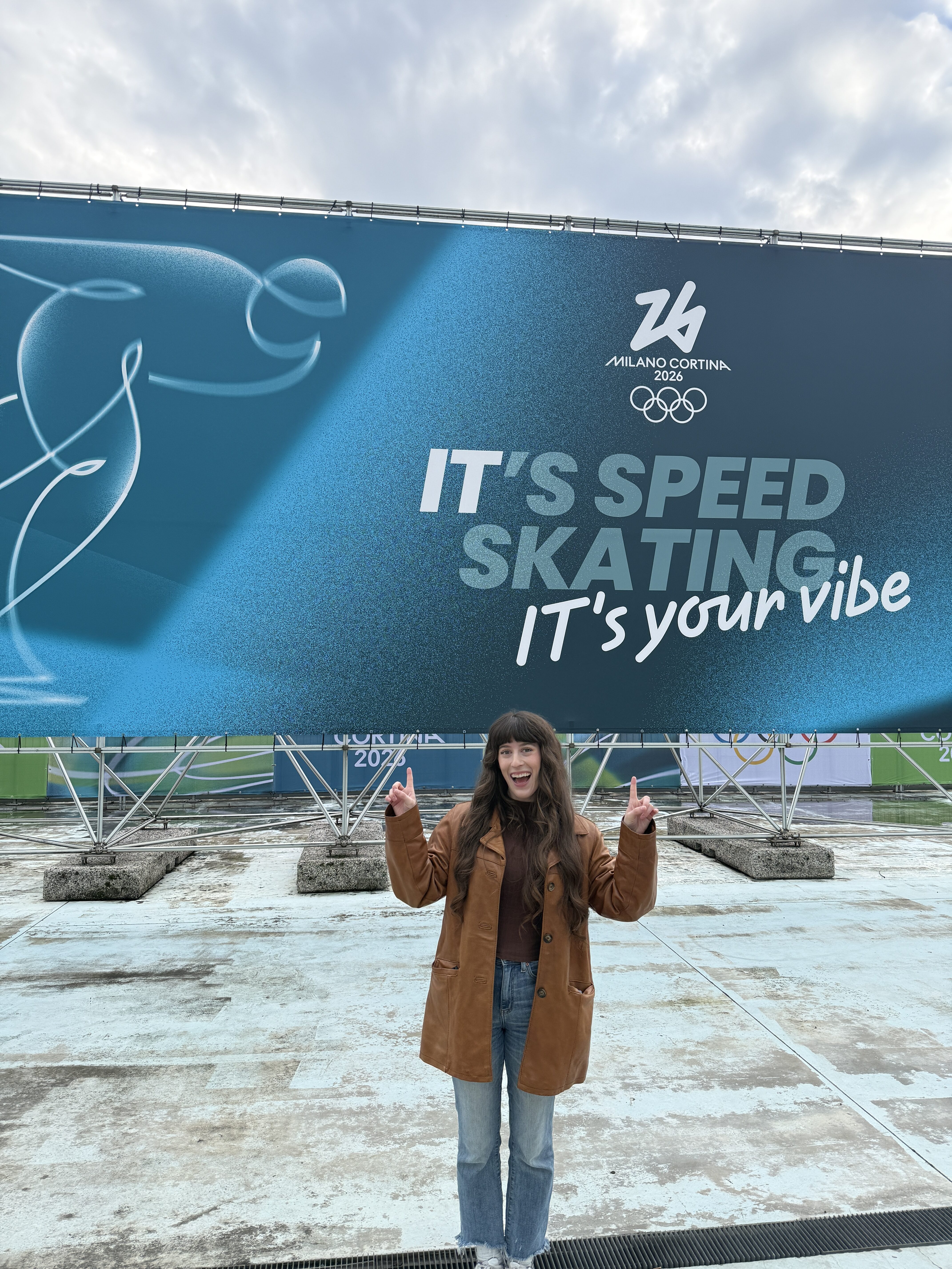 Bella posing in front of the Milano-Cortina 2026 speed skating sign.